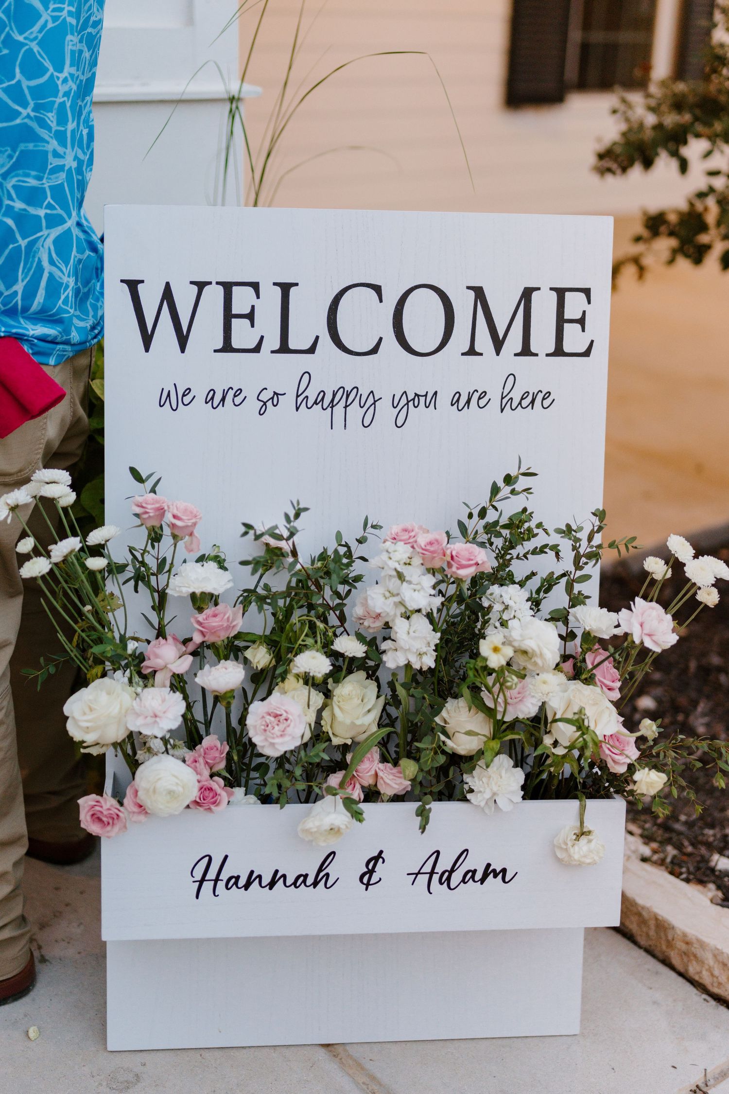 A wedding welcome sign decorated with pink and white roses and delicate floral arrangements.