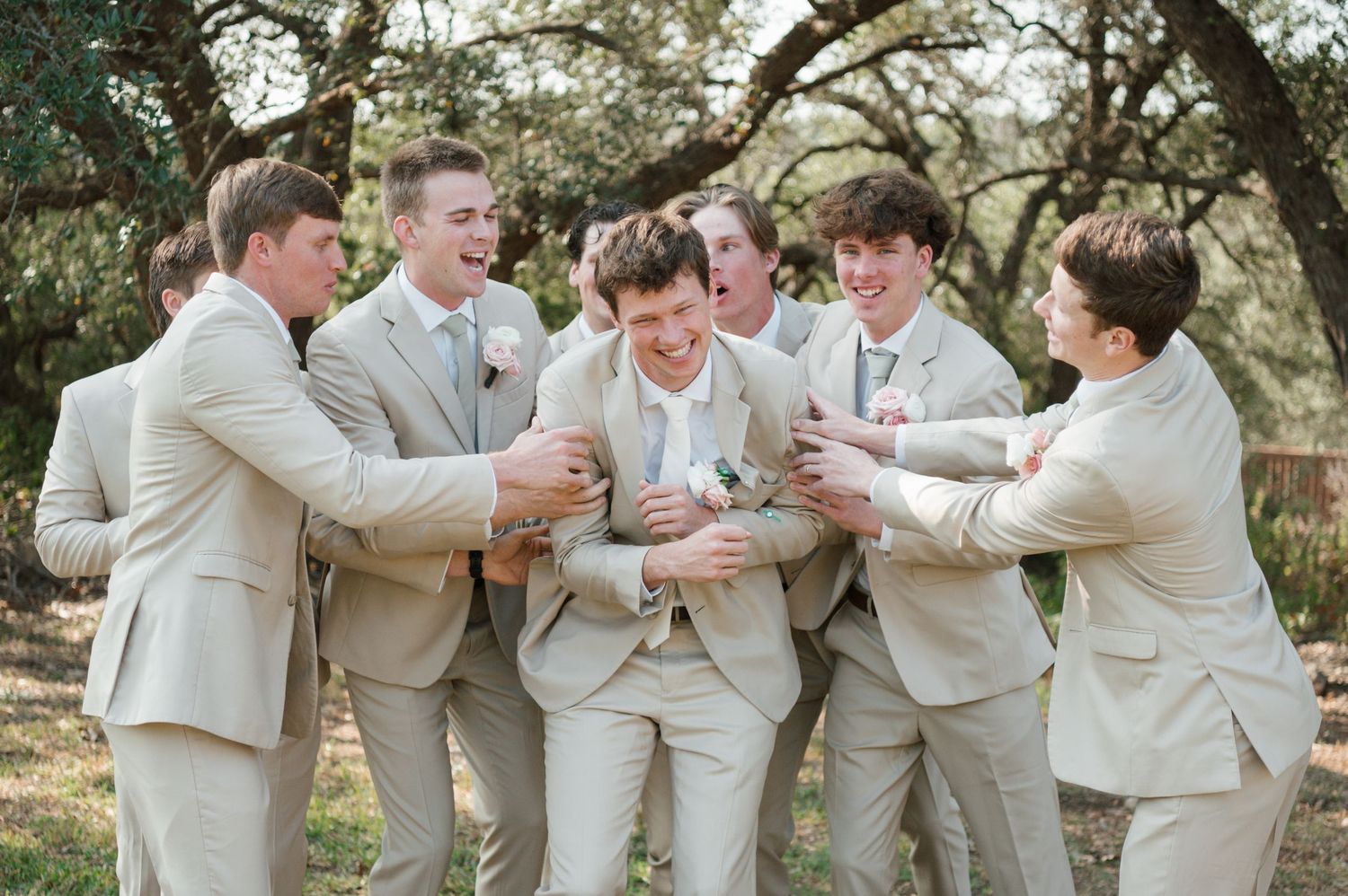 Groomsmen in tan suits share playful moments together during outdoor wedding photo session.