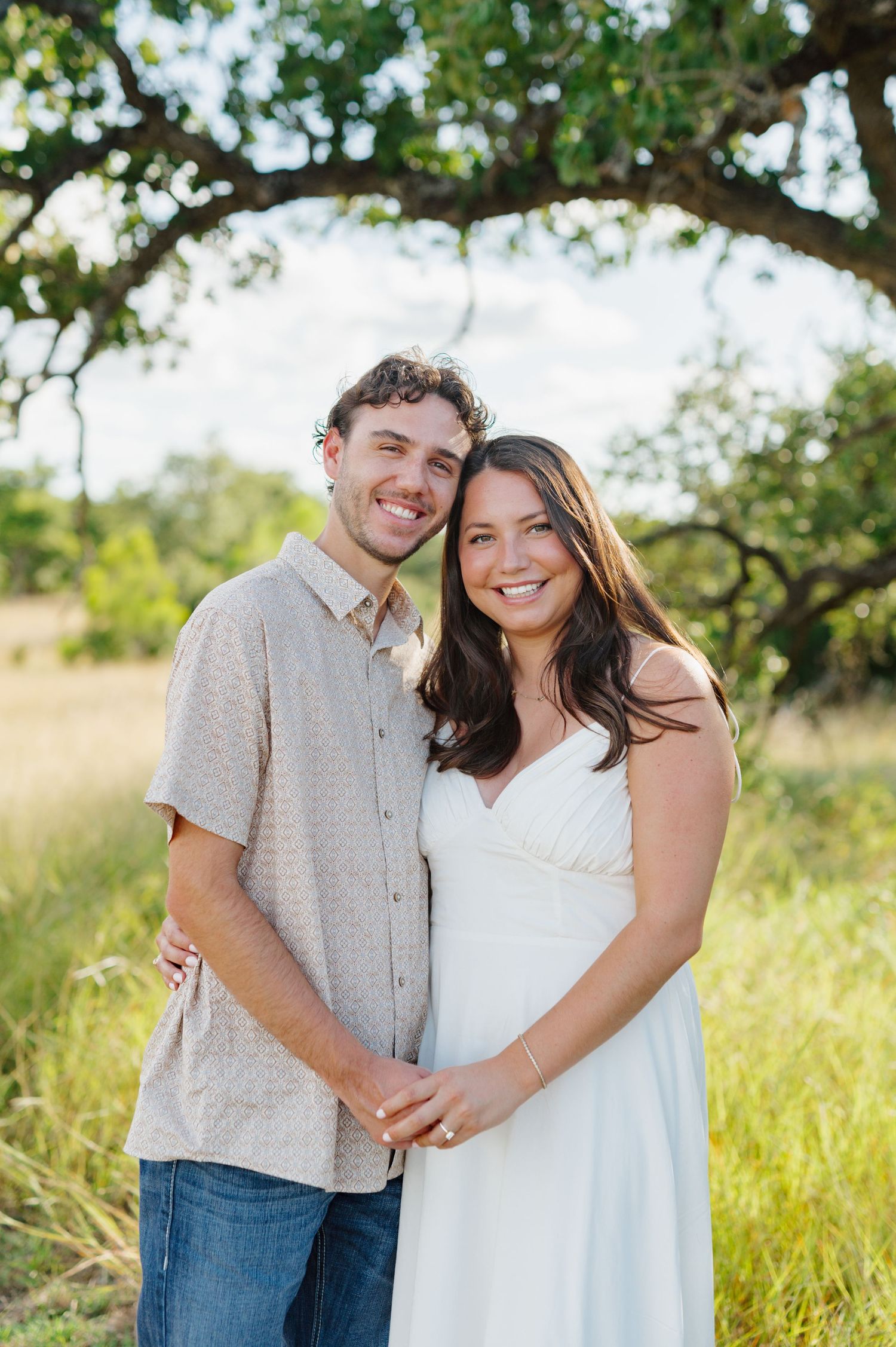 A couple shares a tender moment together in a sun-drenched field with trees in the background.