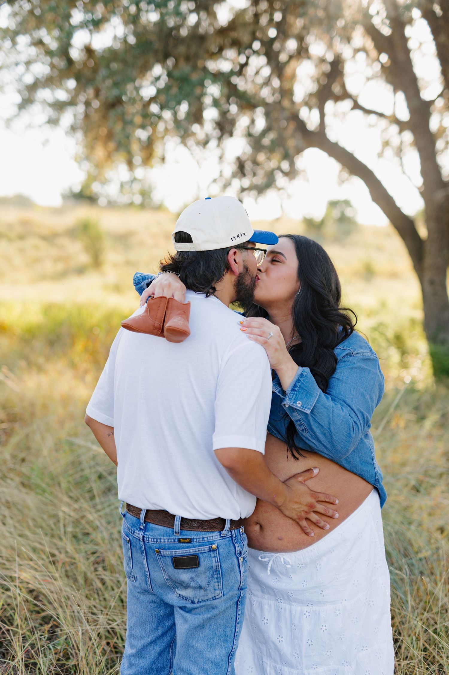 A tender outdoor photoshoot moment with two people in casual denim and white clothing.