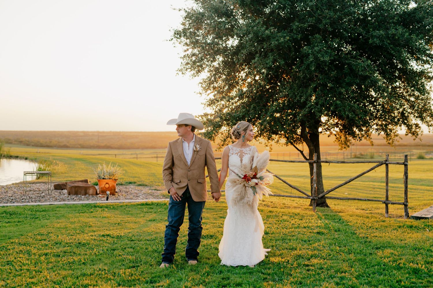 Bride and groom standing together at sunset under tree in rural setting.