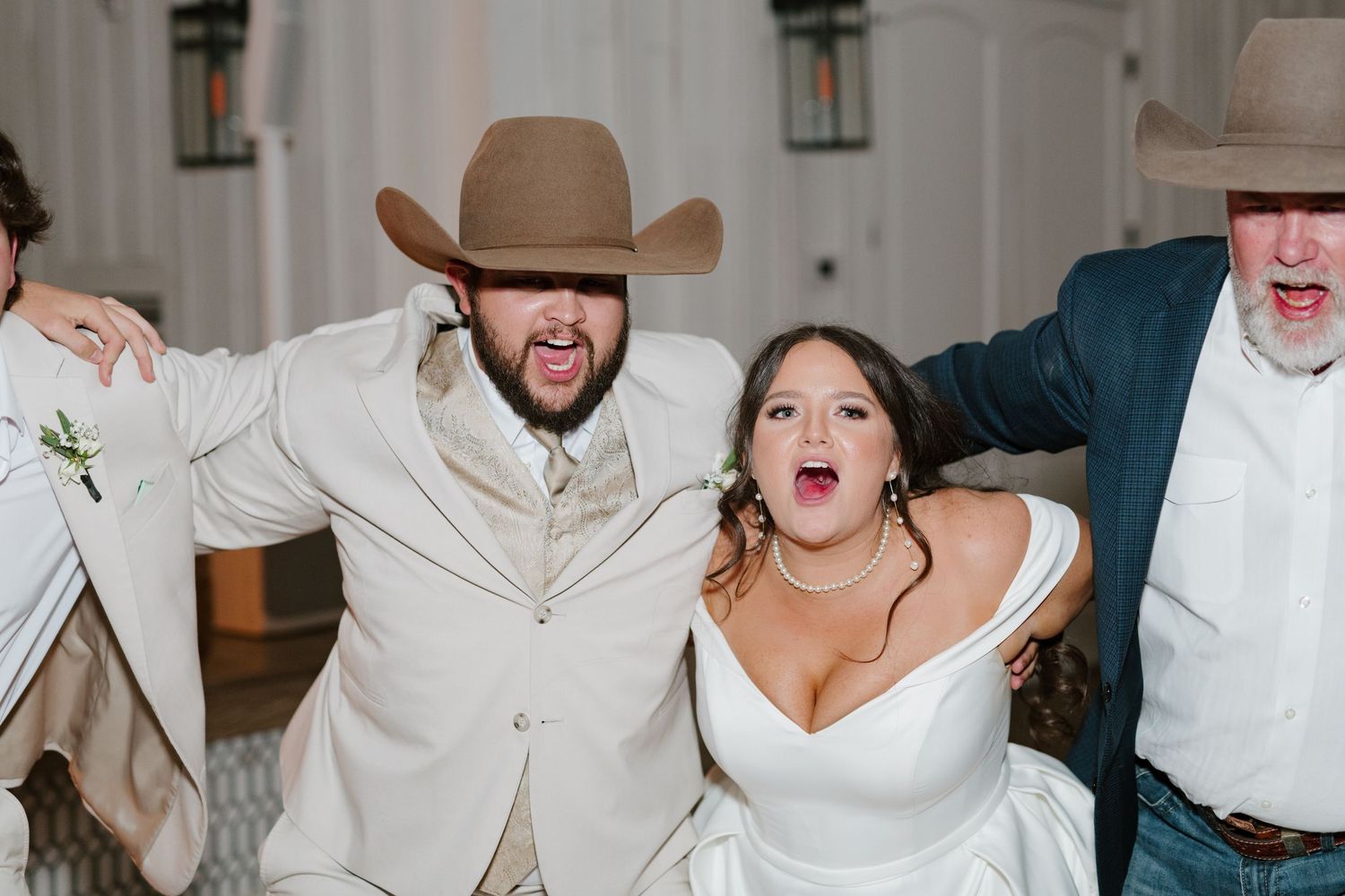 Wedding party members dance together joyfully at reception wearing ivory and white formal attire.