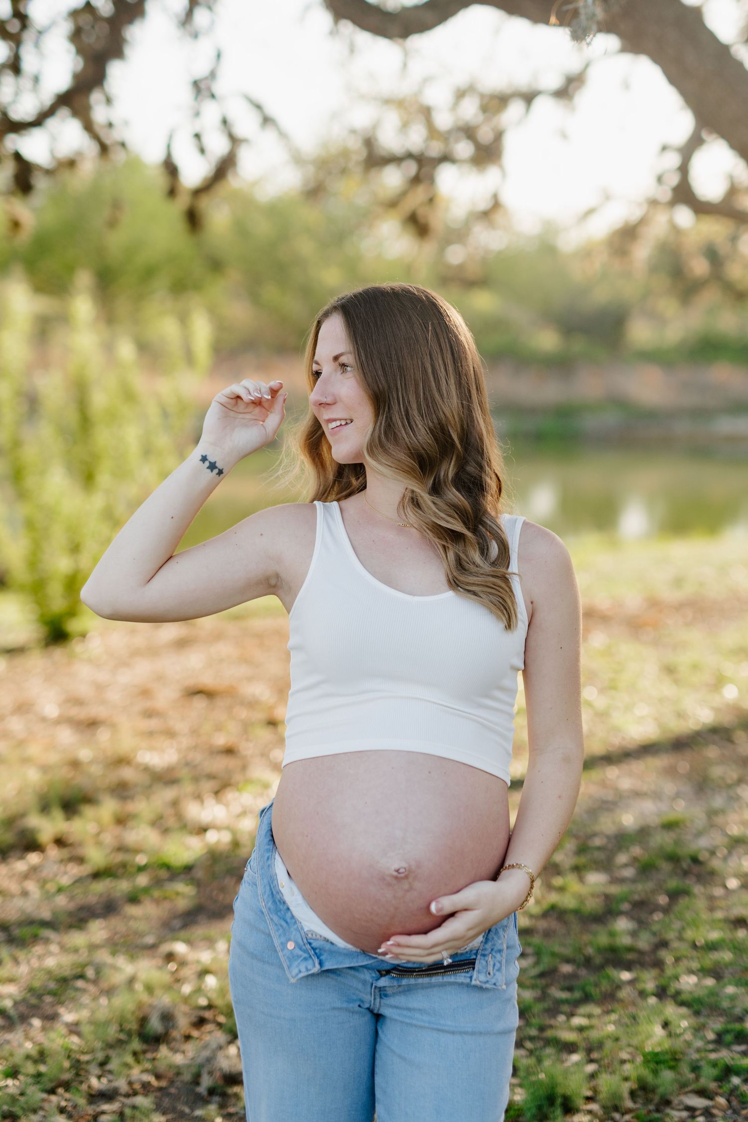Maternity photo of woman in white tank top cradling her baby bump outdoors.