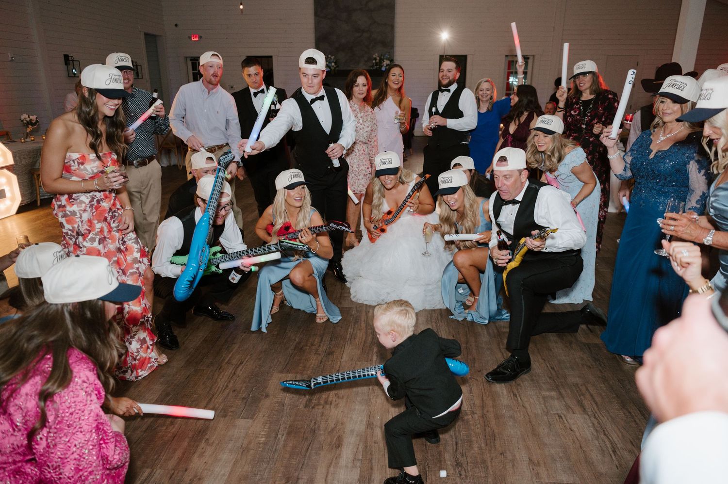 A large group of people dressed in formal attire are gathered together, celebrating and dancing at what appears to be a wedding reception.
