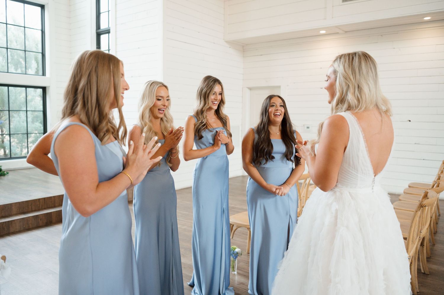 A group of young women in formal dresses are standing together and smiling in a bright, indoor setting.