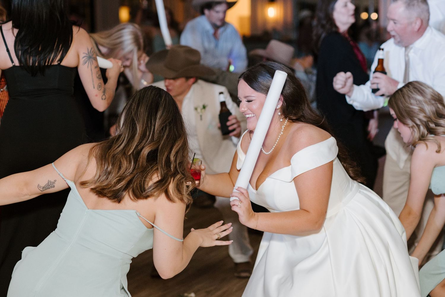 Party goers dance energetically on a dimly lit dance floor during a wedding reception celebration.