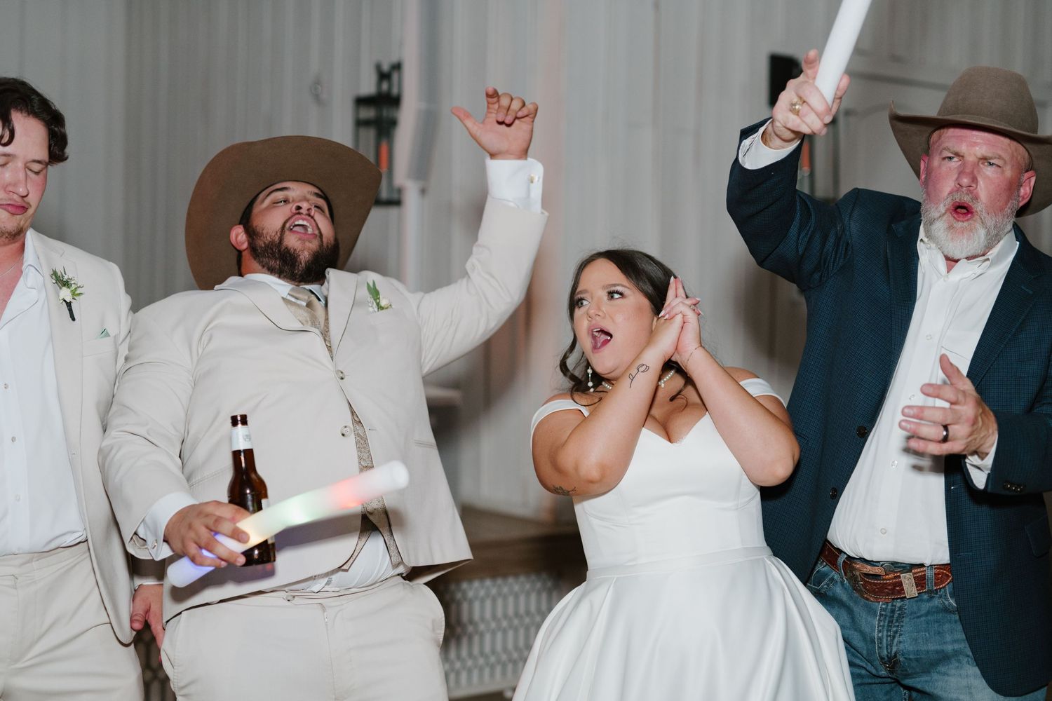 A group of wedding guests and a person in white dress celebrate joyfully together at a lively reception party.