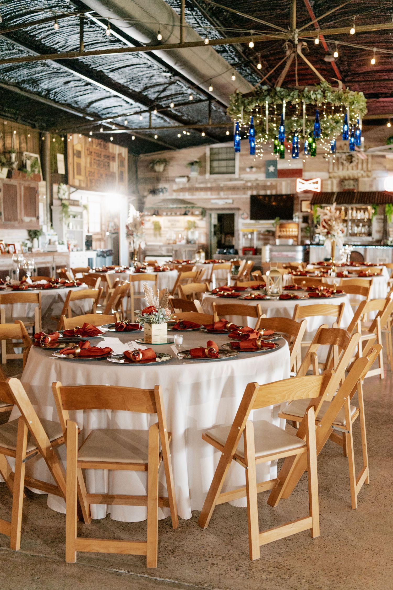 Rustic wedding reception venue with white tablecloths, wooden folding chairs, and hanging greenery chandelier.