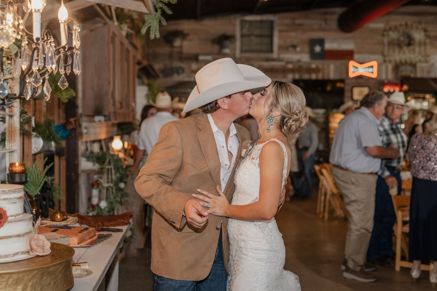 A couple shares a romantic dance moment under a crystal chandelier in a rustic venue setting.