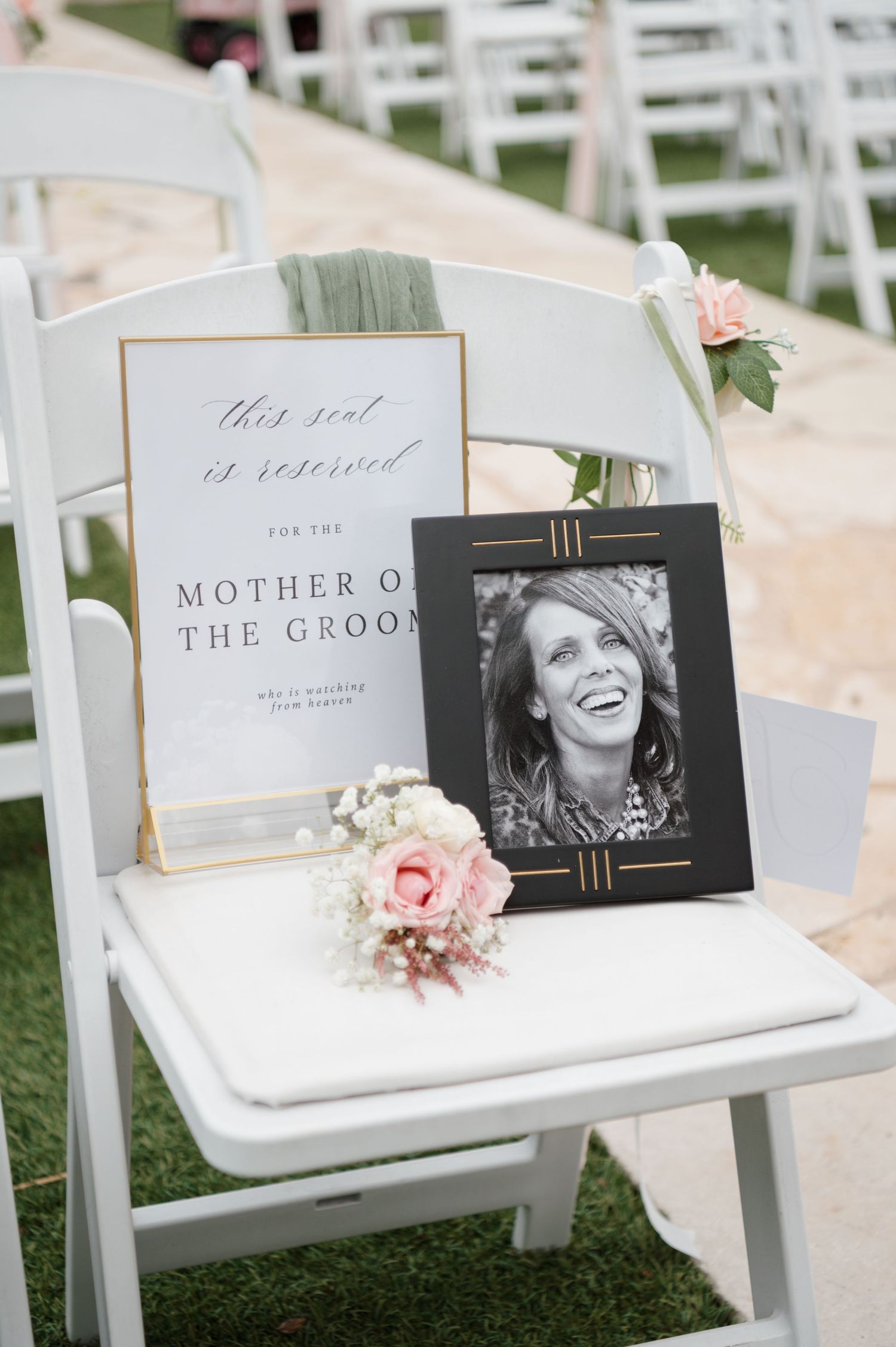 White folding chairs display framed photos and signs for wedding ceremony seating on a grass lawn.