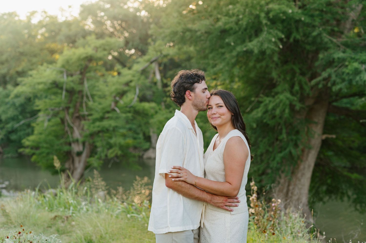 A couple shares romantic moments during a summer photoshoot among lush green trees.