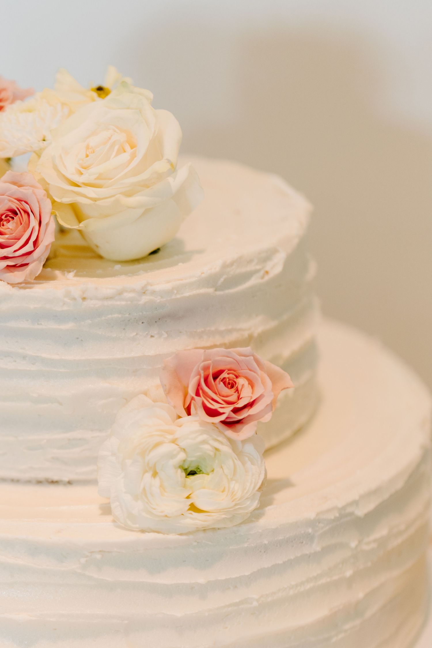 Delicate white wedding cake decorated with fresh pink and cream roses on pale background.