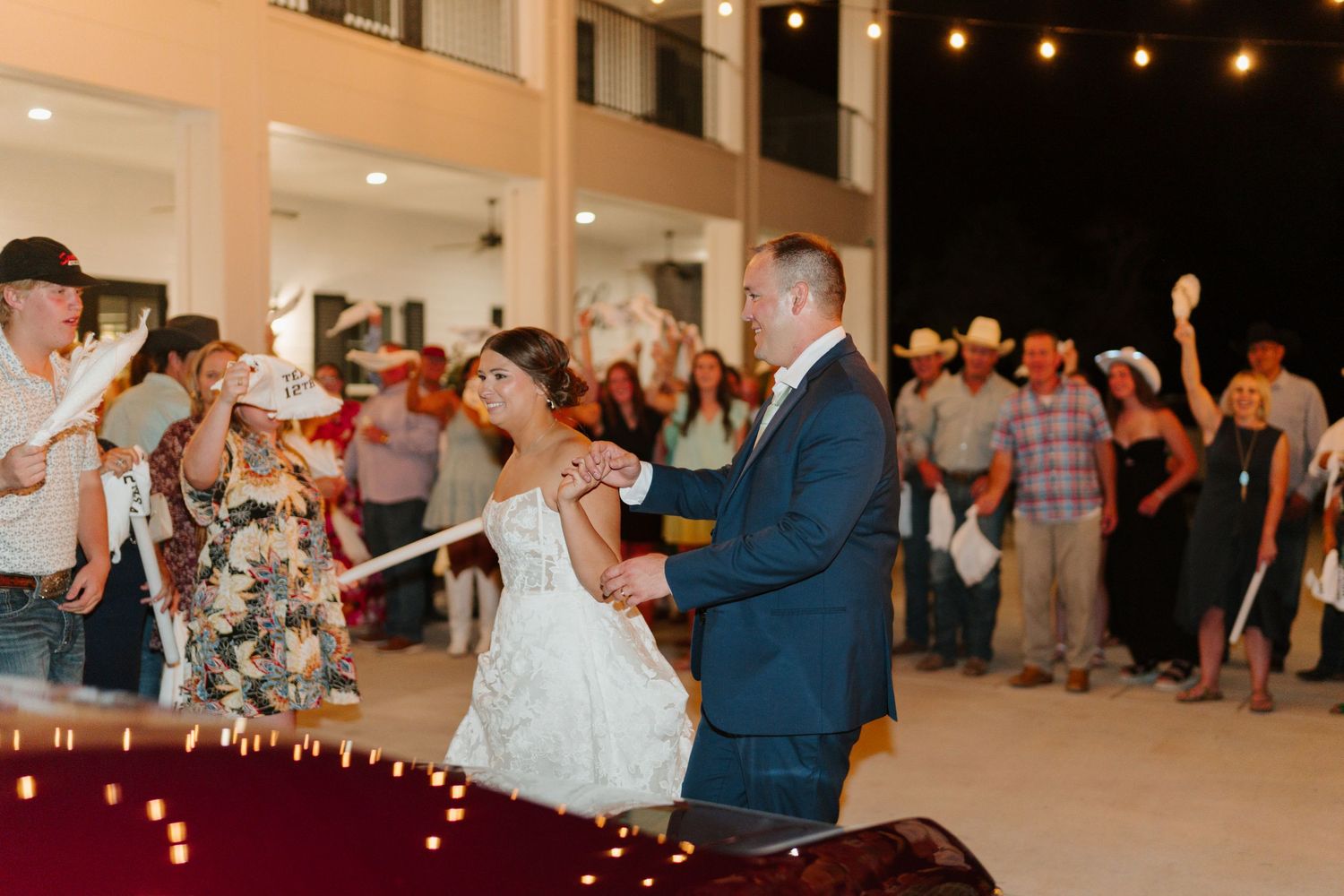 Wedding couple dancing surrounded by celebrating guests under string lights.
