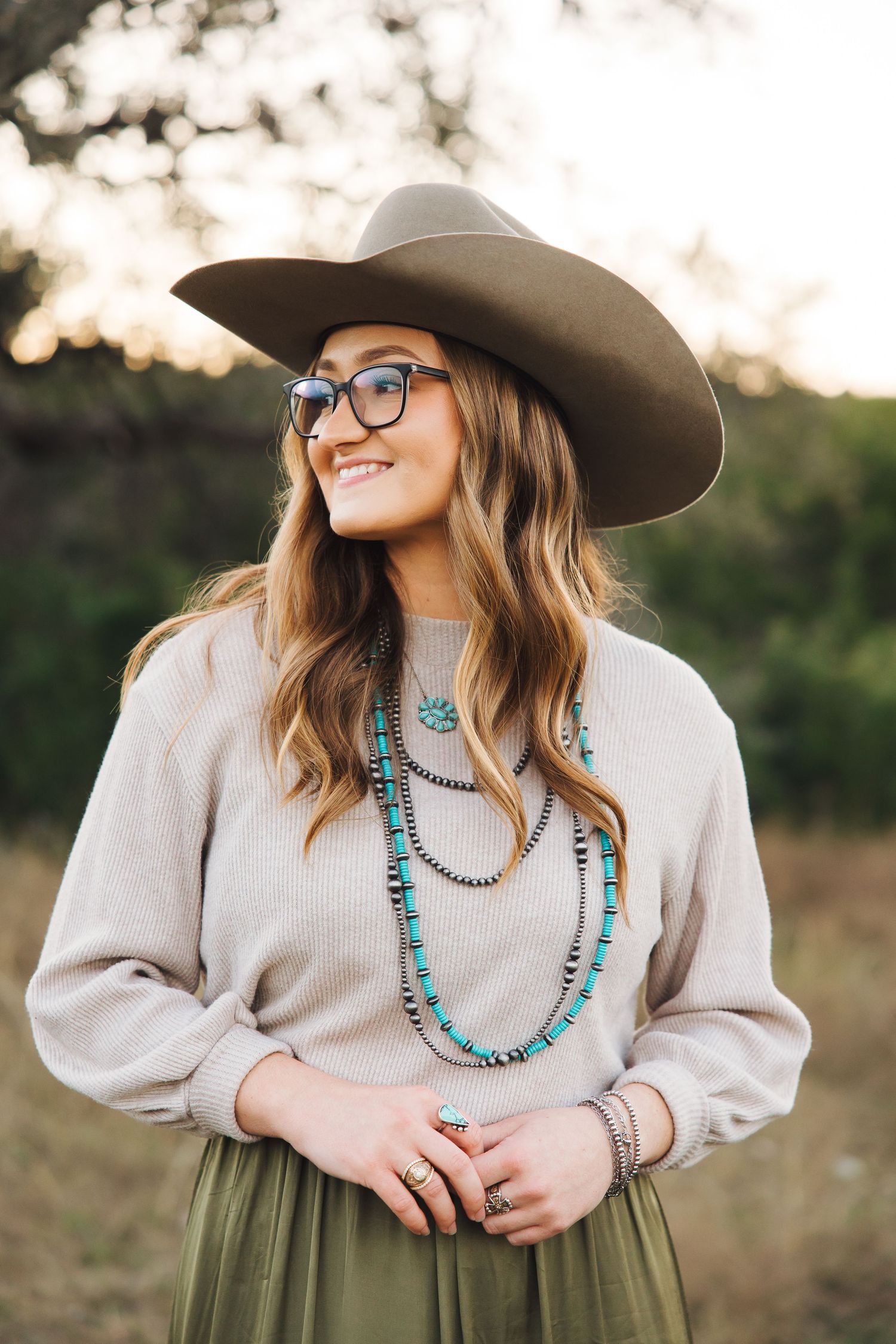 Western style portrait featuring turquoise jewelry, cowboy hat, and cozy sweater in an outdoor setting.