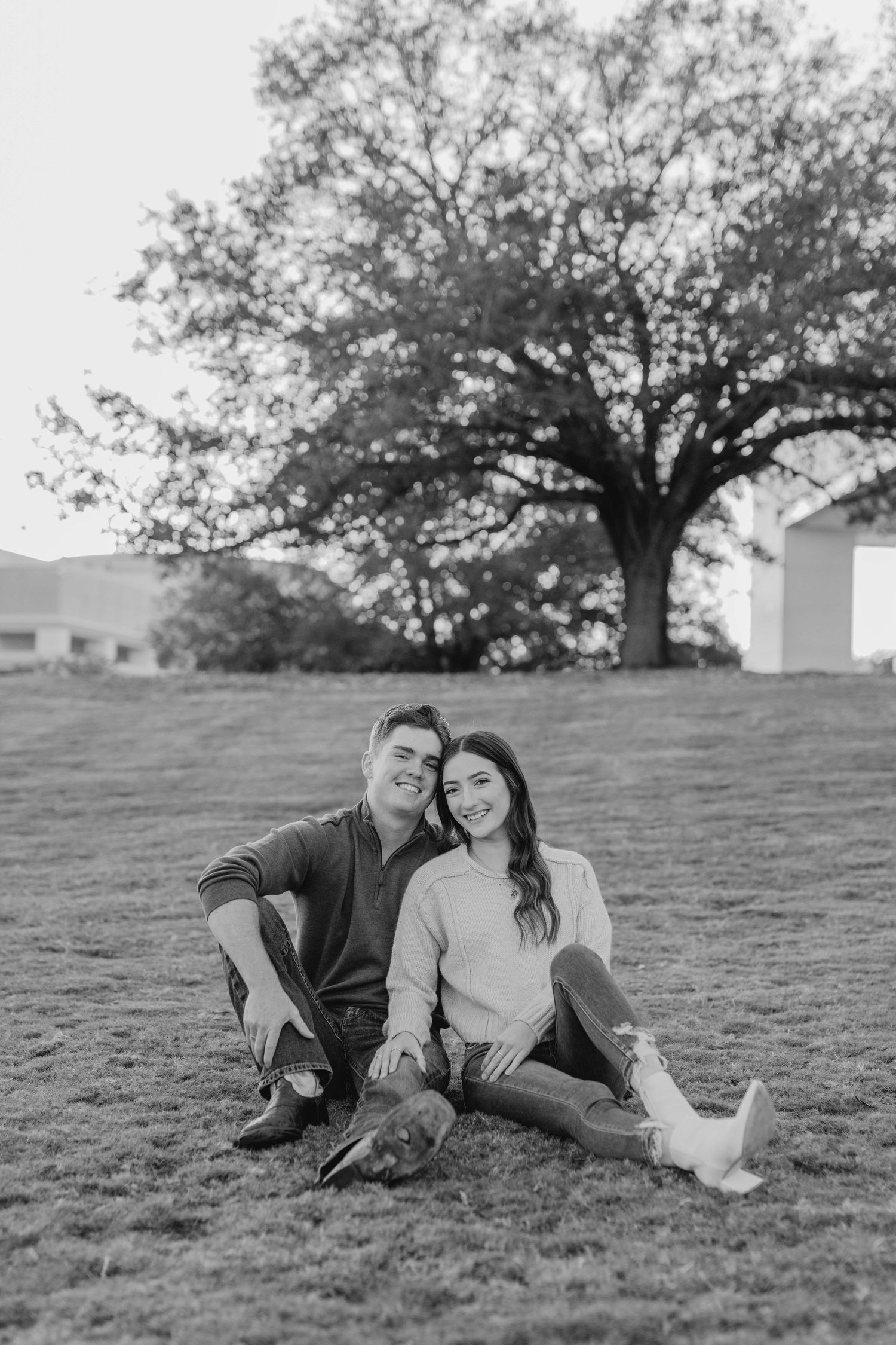 A black and white photo of a couple sitting together on a grassy hillside.