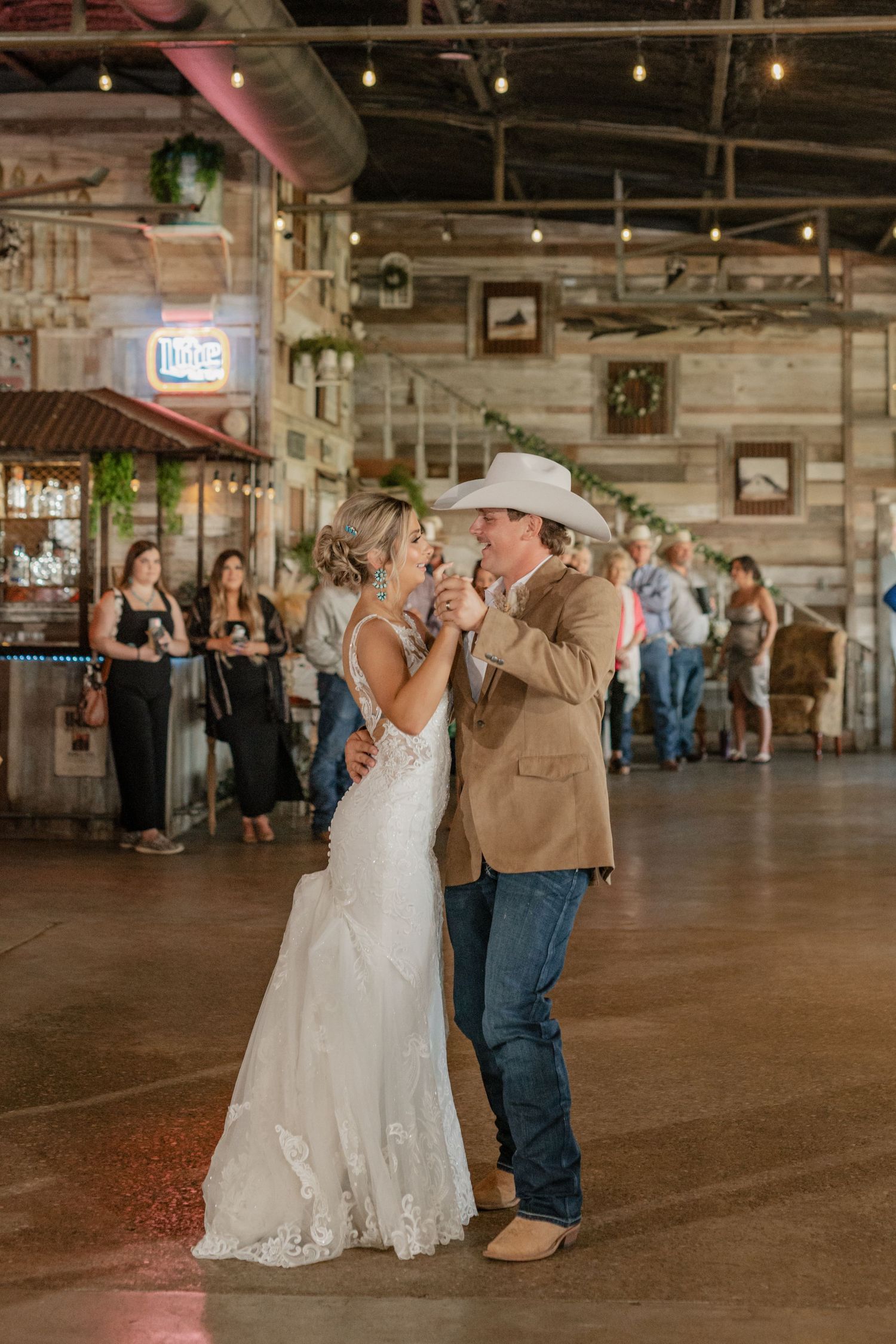 Dancing the first dance as newlyweds in a rustic barn venue with string lights overhead.