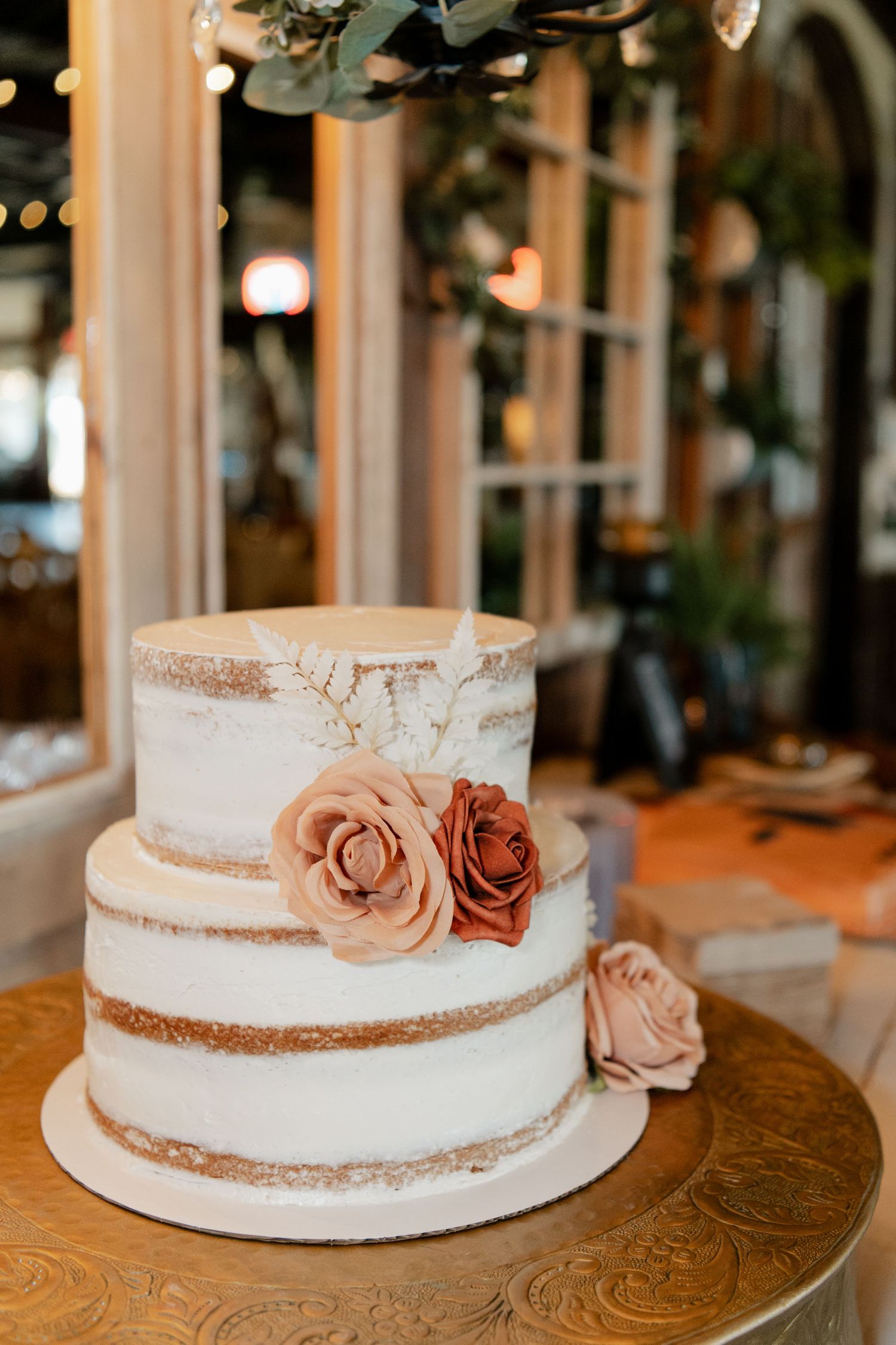A semi-naked wedding cake decorated with dusty rose flowers on a wooden table.