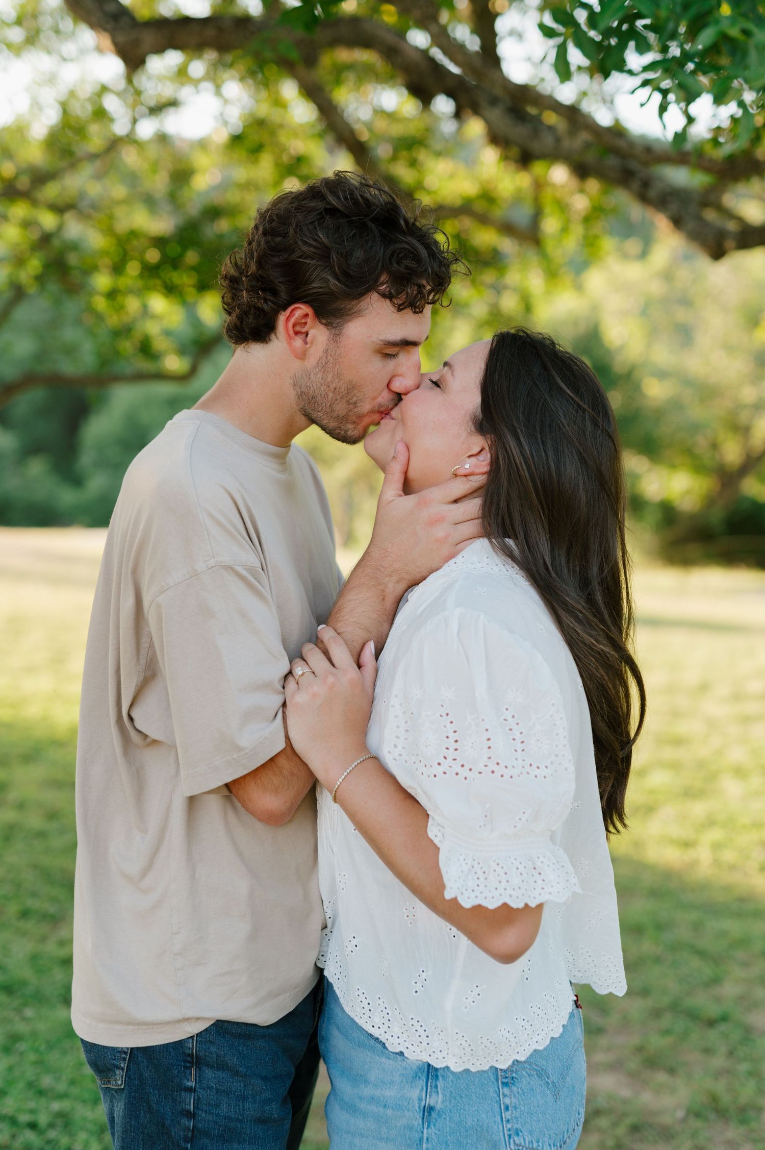 A romantic moment captured between a couple in denim and light colored tops against a natural outdoor backdrop.