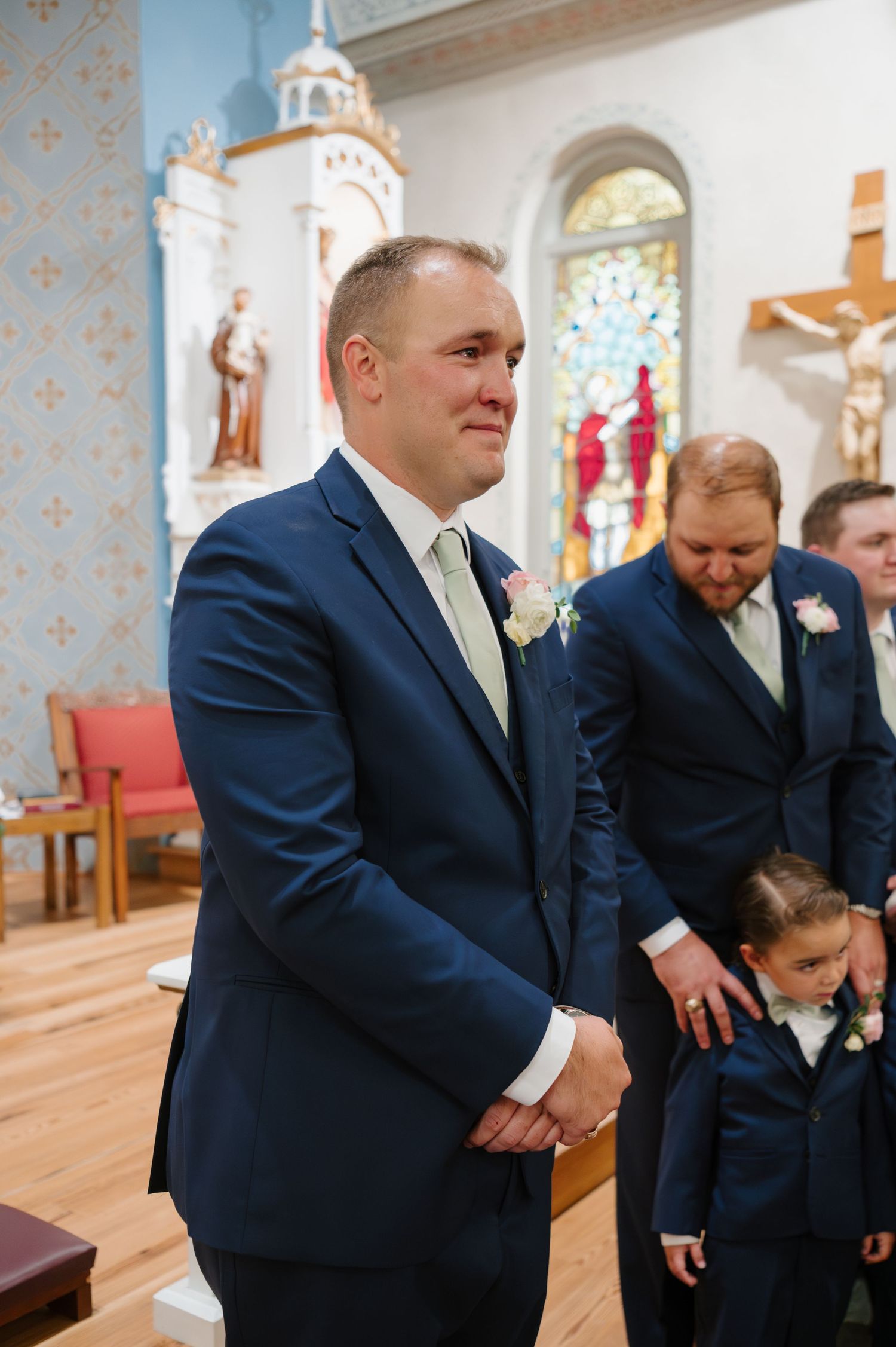 Wedding party members in navy suits stand together inside a traditional church sanctuary.