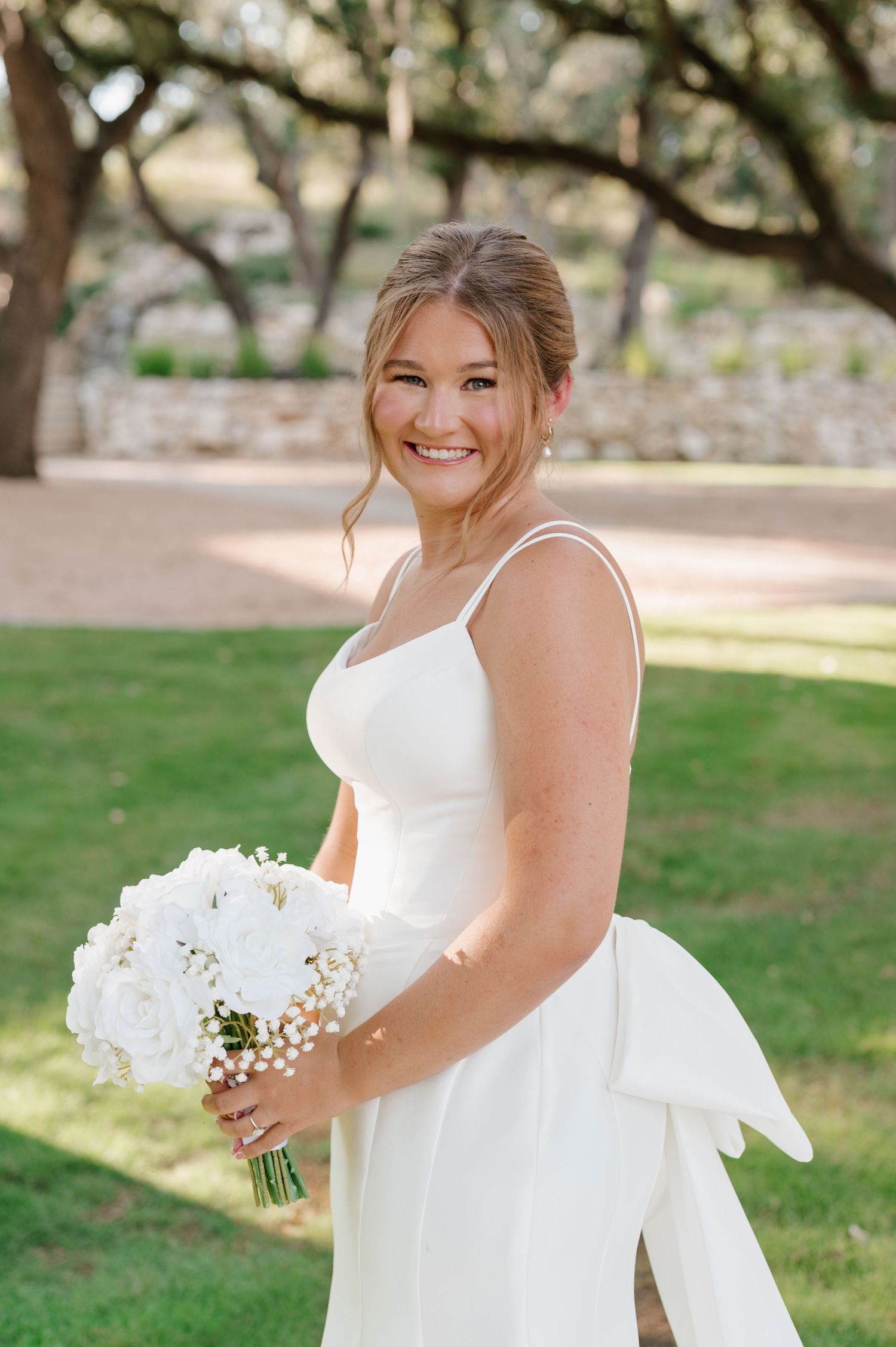 Bride holds white bouquet while posing in an elegant wedding dress outdoors.