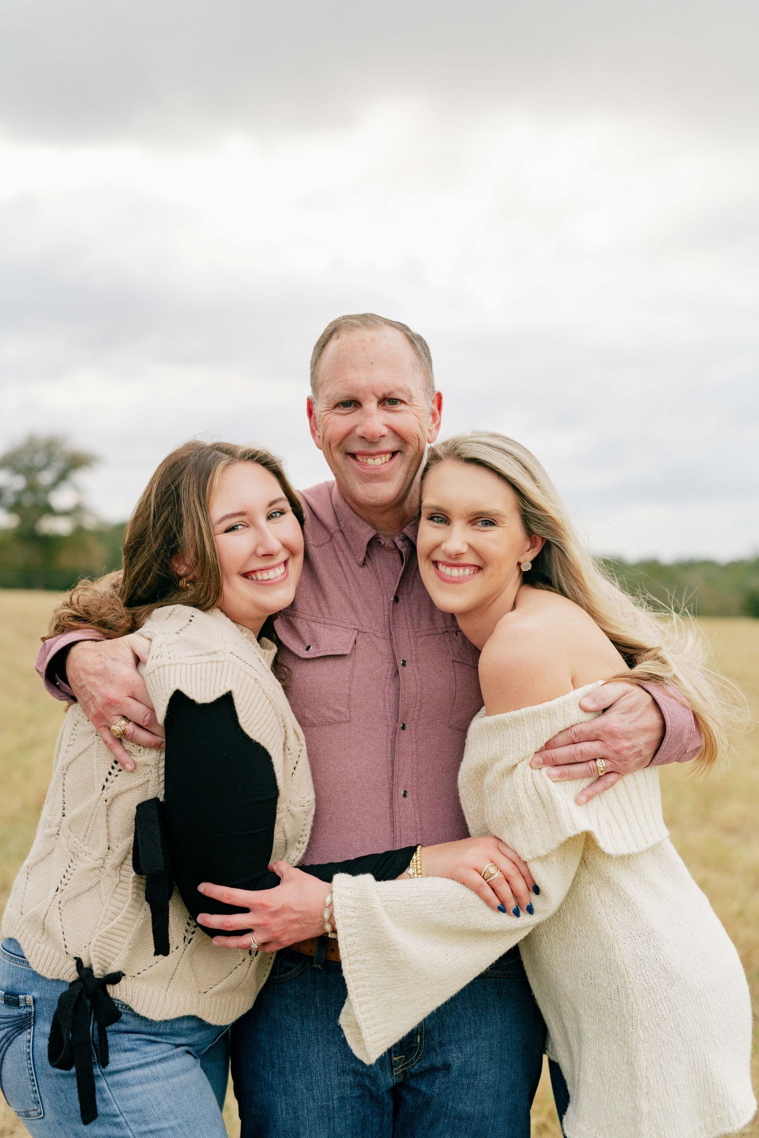 Close-up portrait of three people hugging and smiling in an open field.