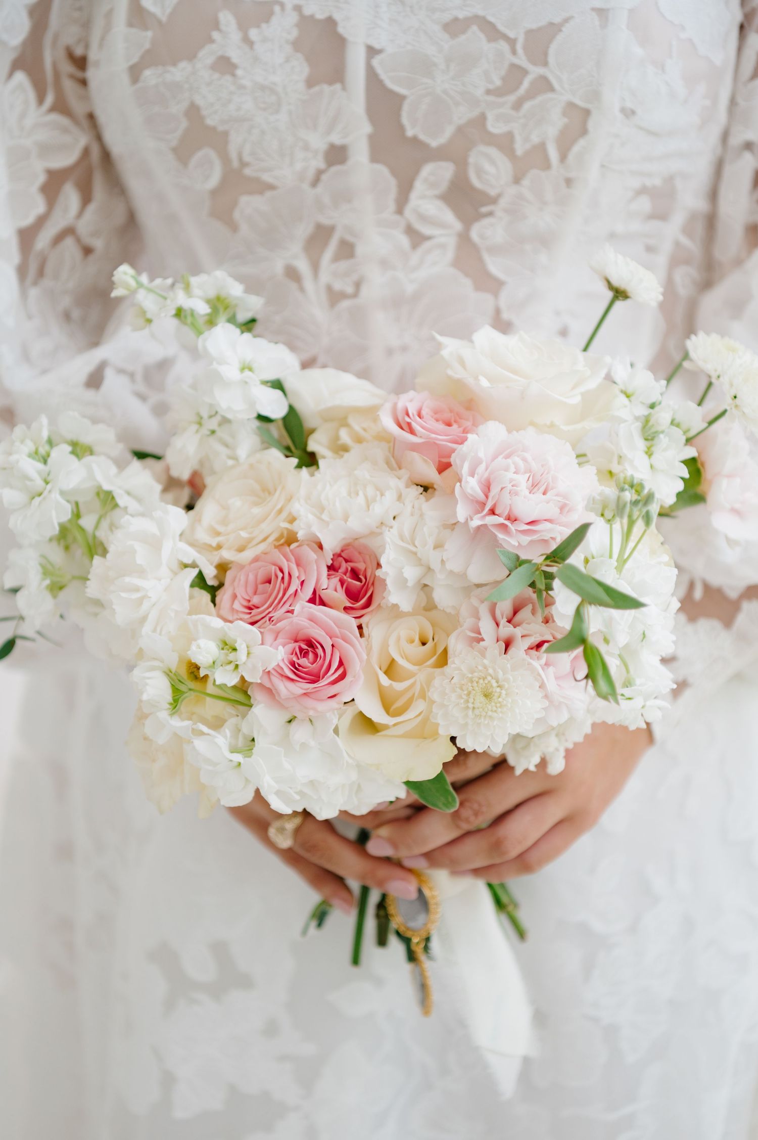 Delicate bouquet of pink roses and white flowers against lace backdrop.