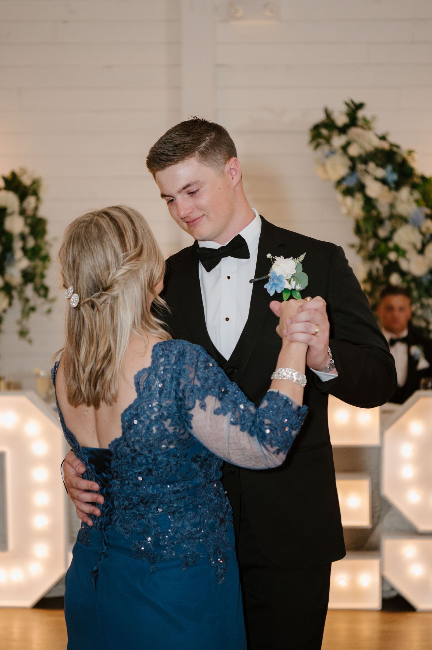 A couple dancing at a formal event, the woman wearing a blue sequined dress and the man in a tuxedo.
