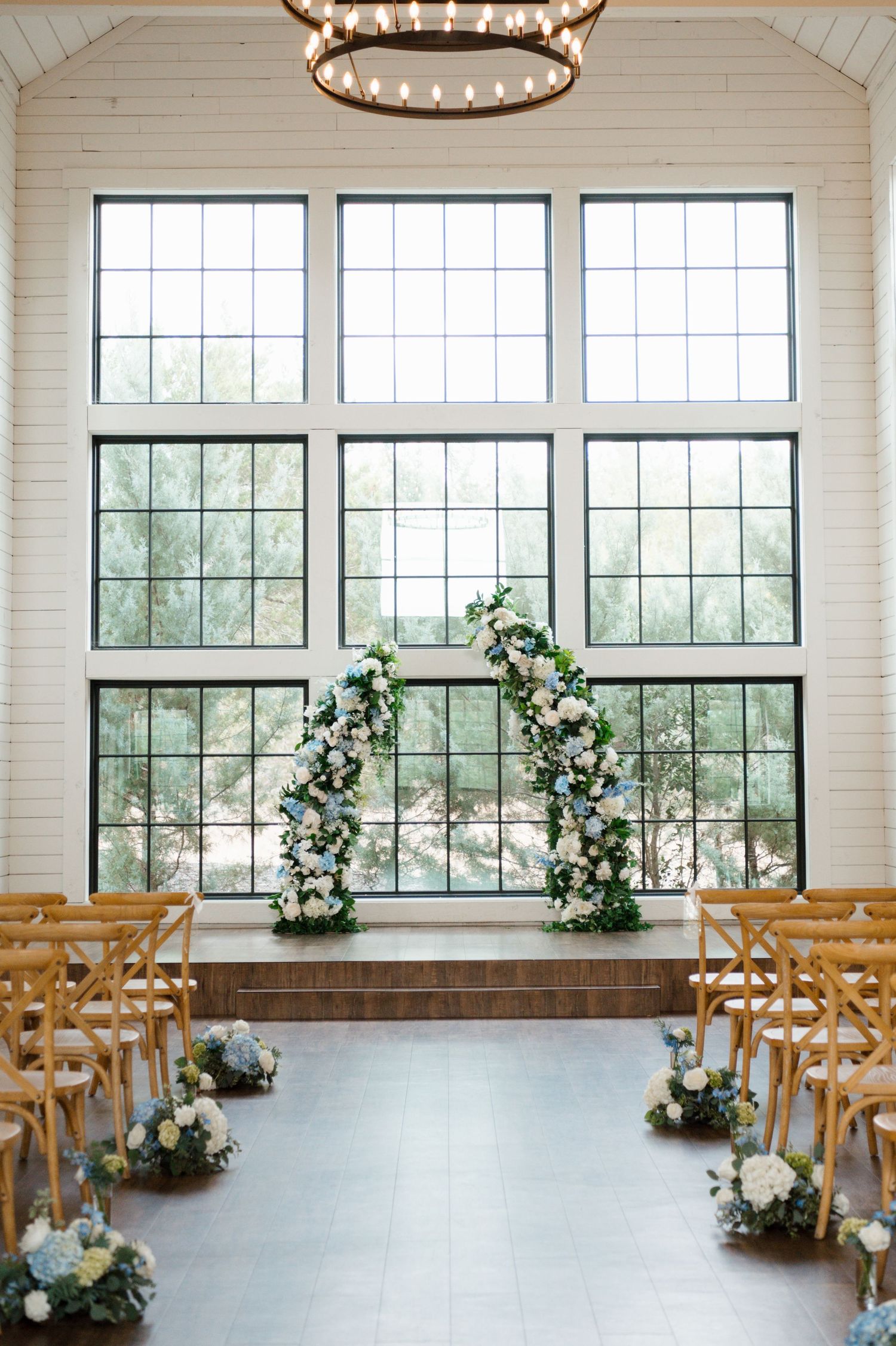 A wedding ceremony venue with large windows, floral decorations, and wooden benches.