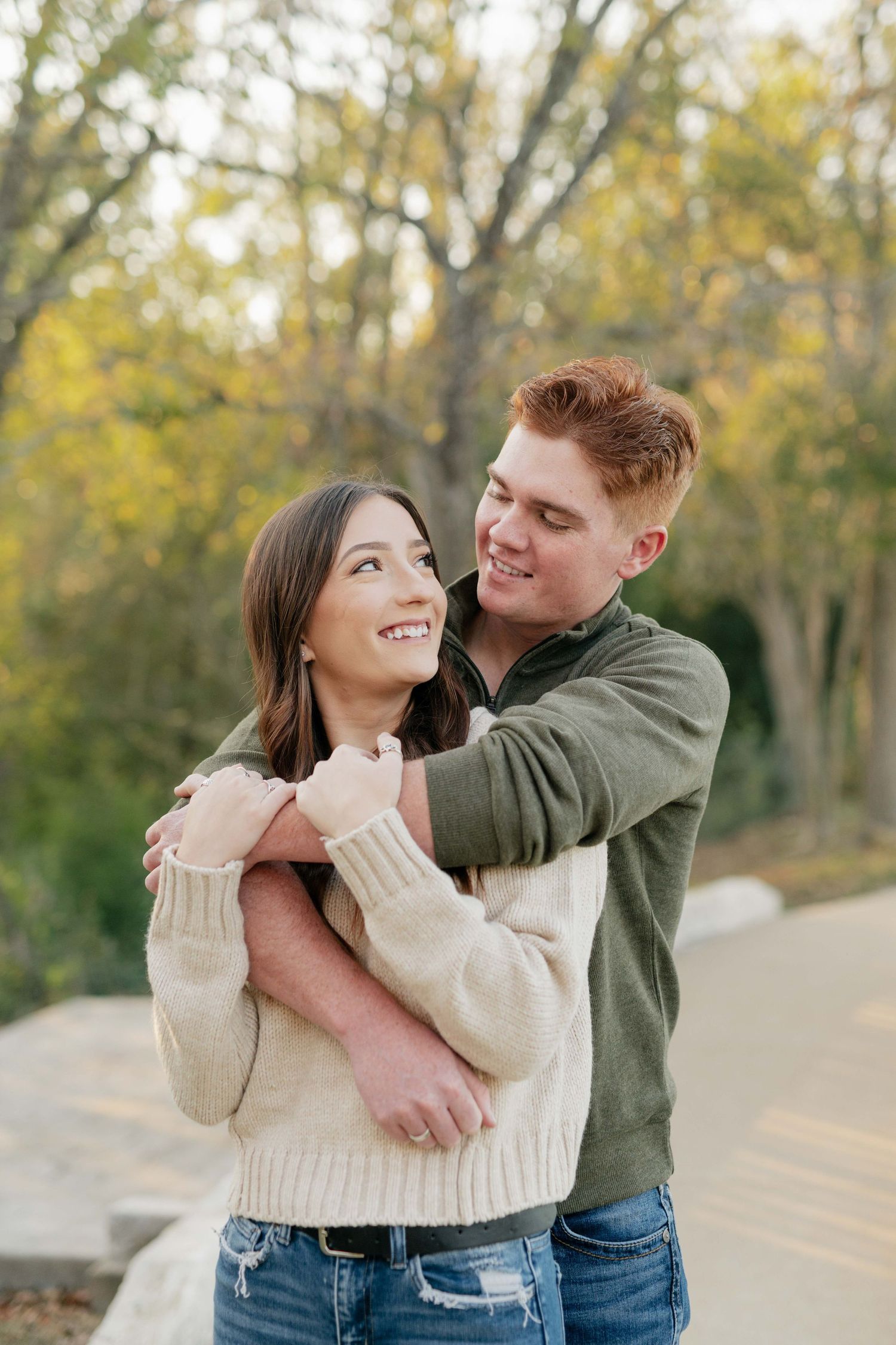A couple shares a tender moment while hugging on a path surrounded by fall foliage.