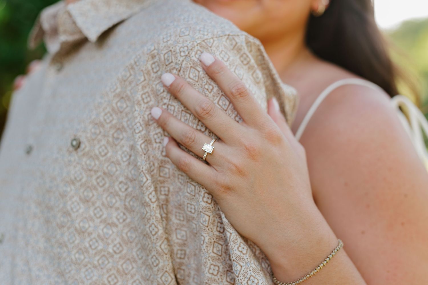 Close-up shot of hands wearing a diamond engagement ring and silver bracelet against a cream-colored dress.