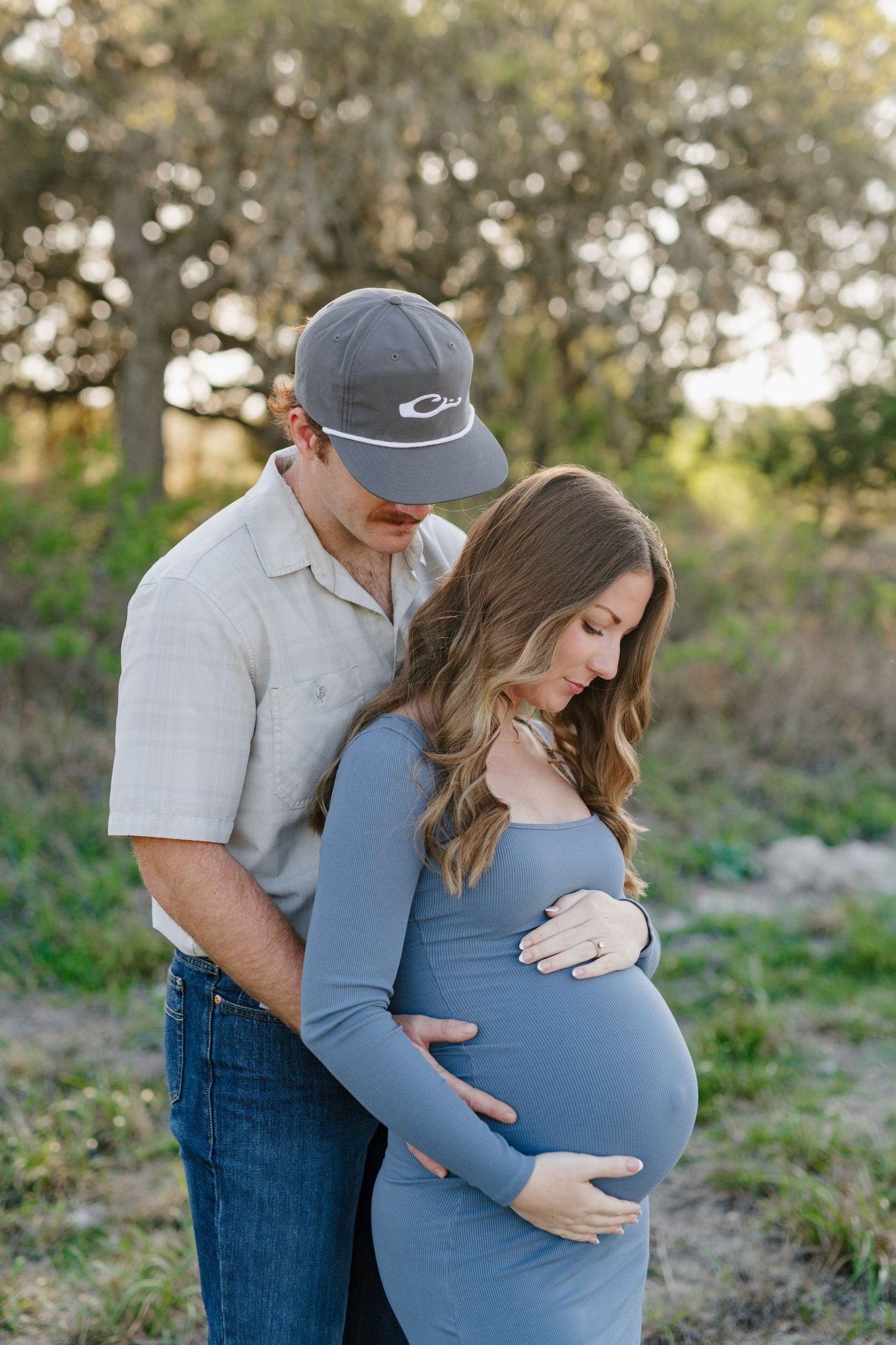 A couple embraces outdoors in a romantic maternity photo shoot featuring a blue dress and casual attire.