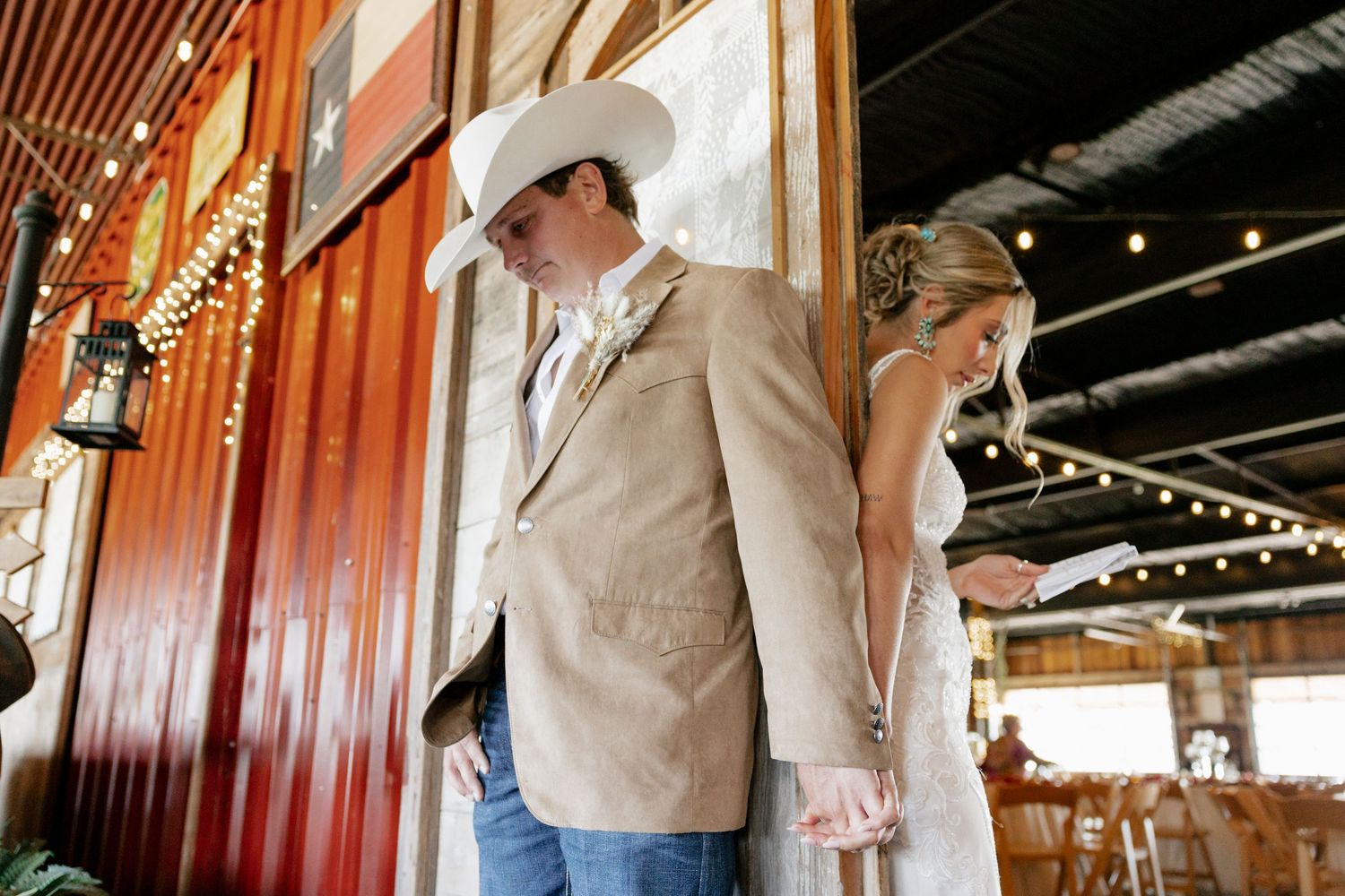 Couple in western wedding attire standing back to back in rustic wooden venue.
