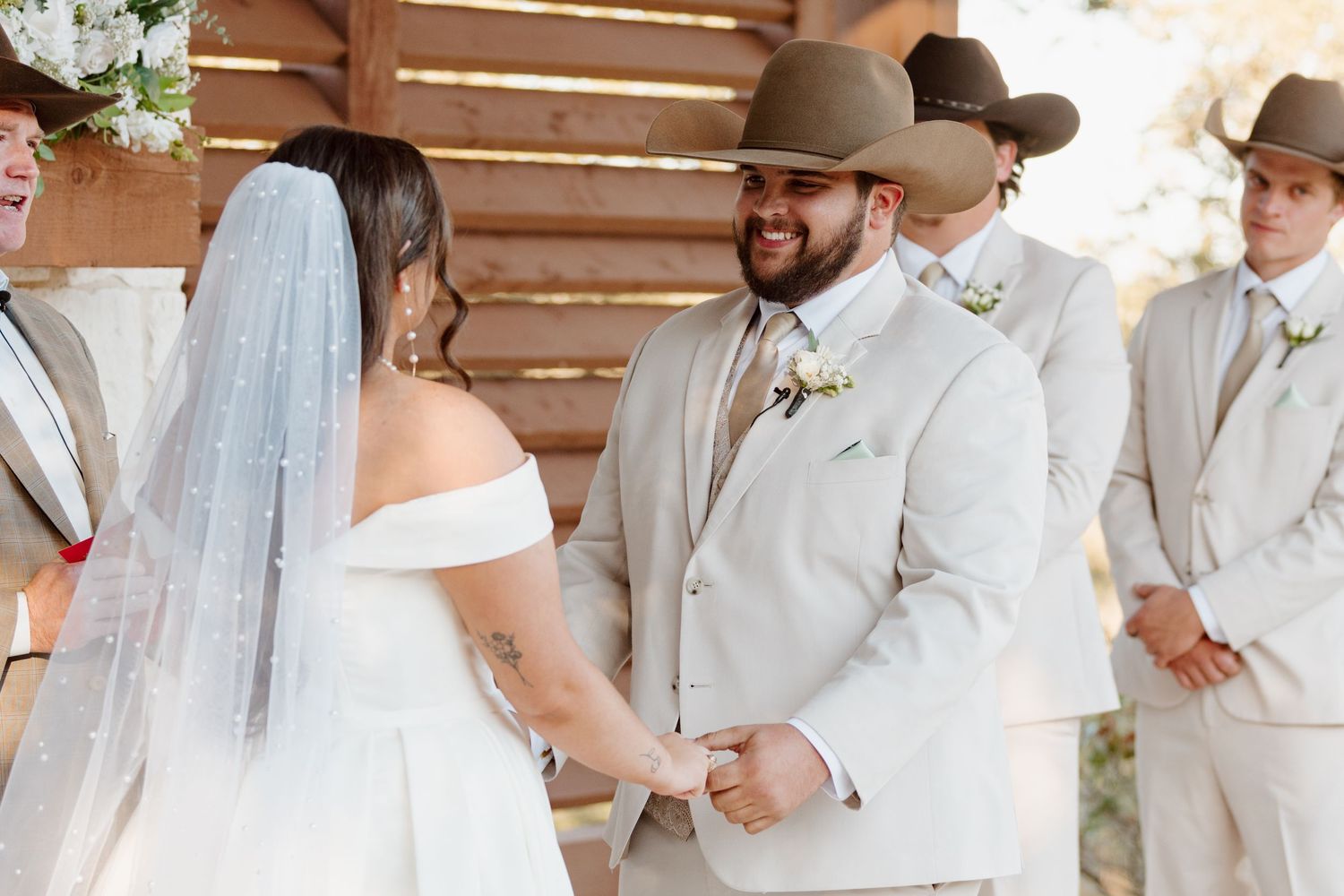 Beautiful outdoor wedding ceremony with the couple exchanging rings in front of a rustic wooden backdrop.
