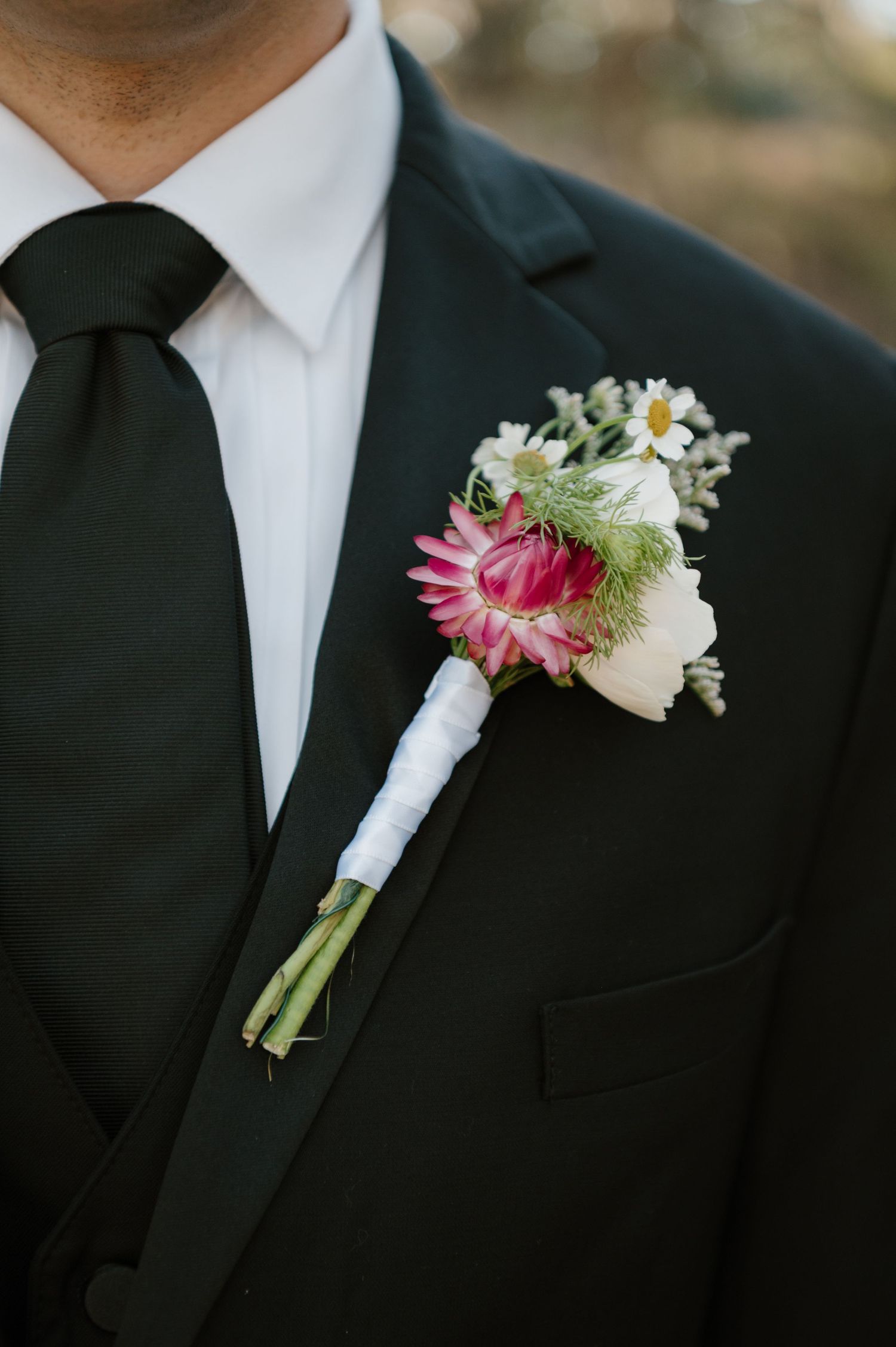 Close-up of pink and white floral boutonniere on black suit lapel.