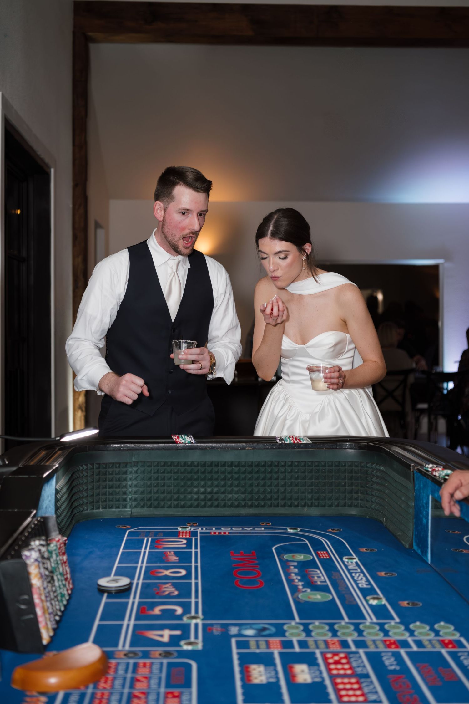 Couple in formal wedding attire playing craps at a casino table during their reception celebration.