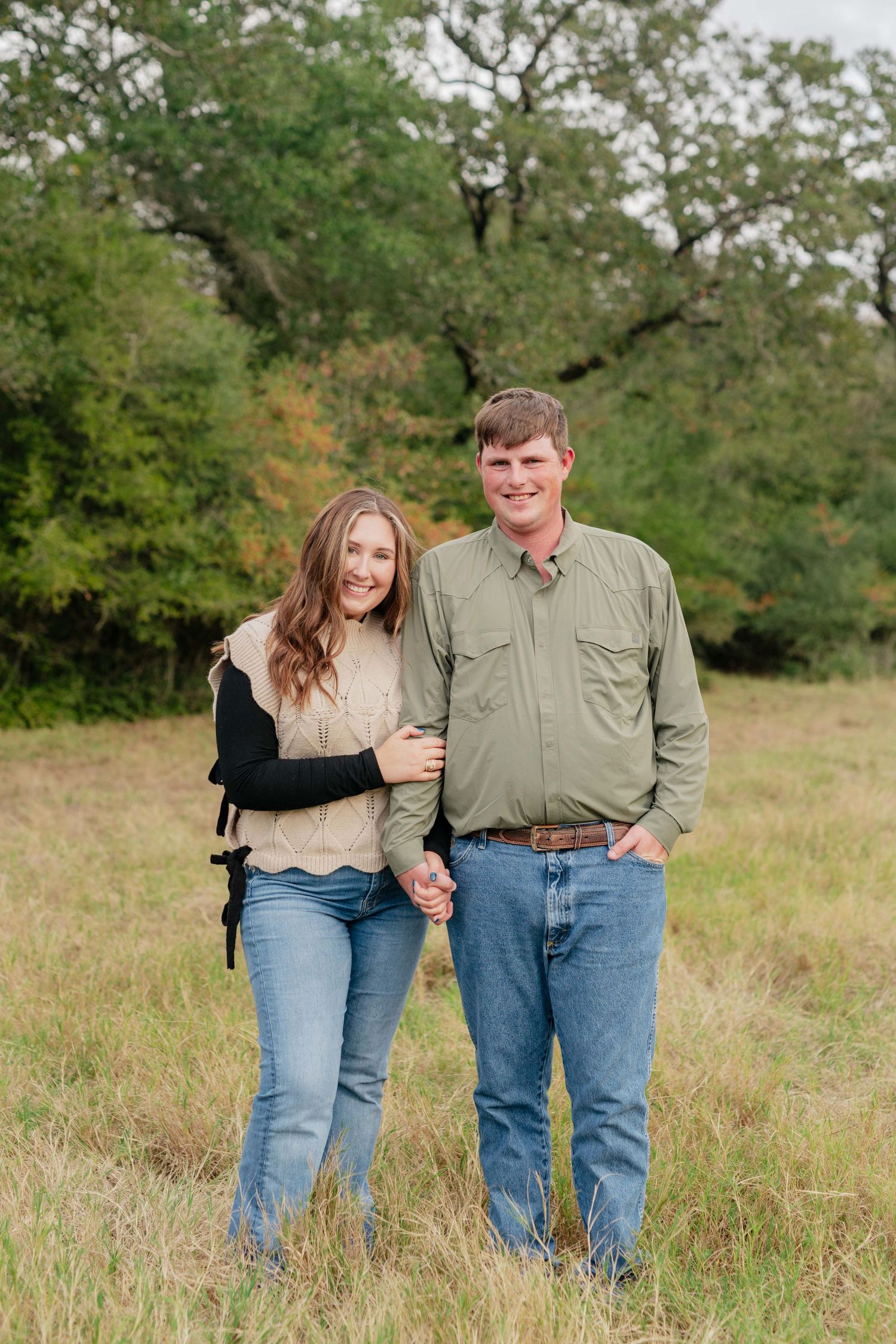 A couple stands together in a rustic field setting.