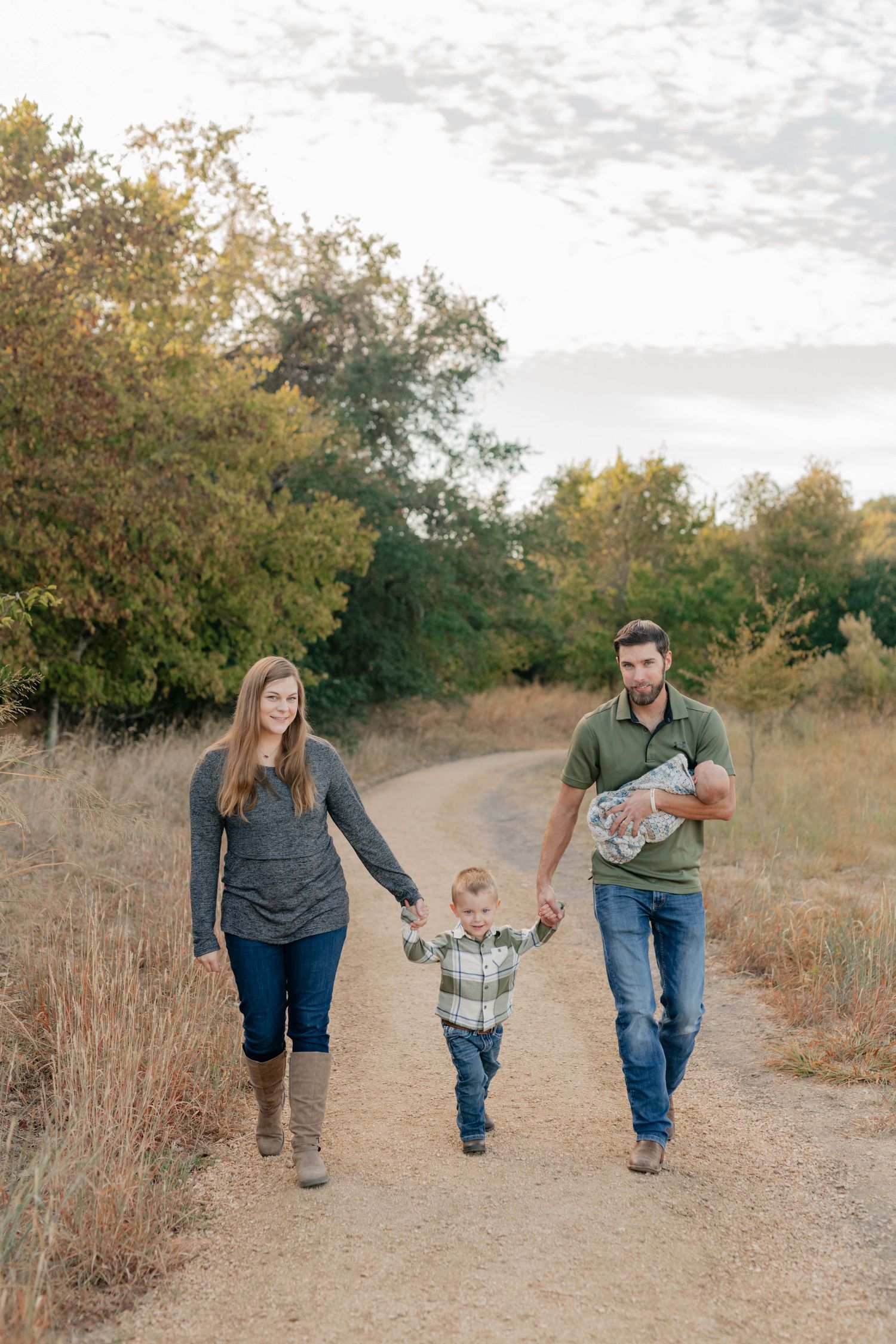 Family walking together on a dirt path through autumn scenery.