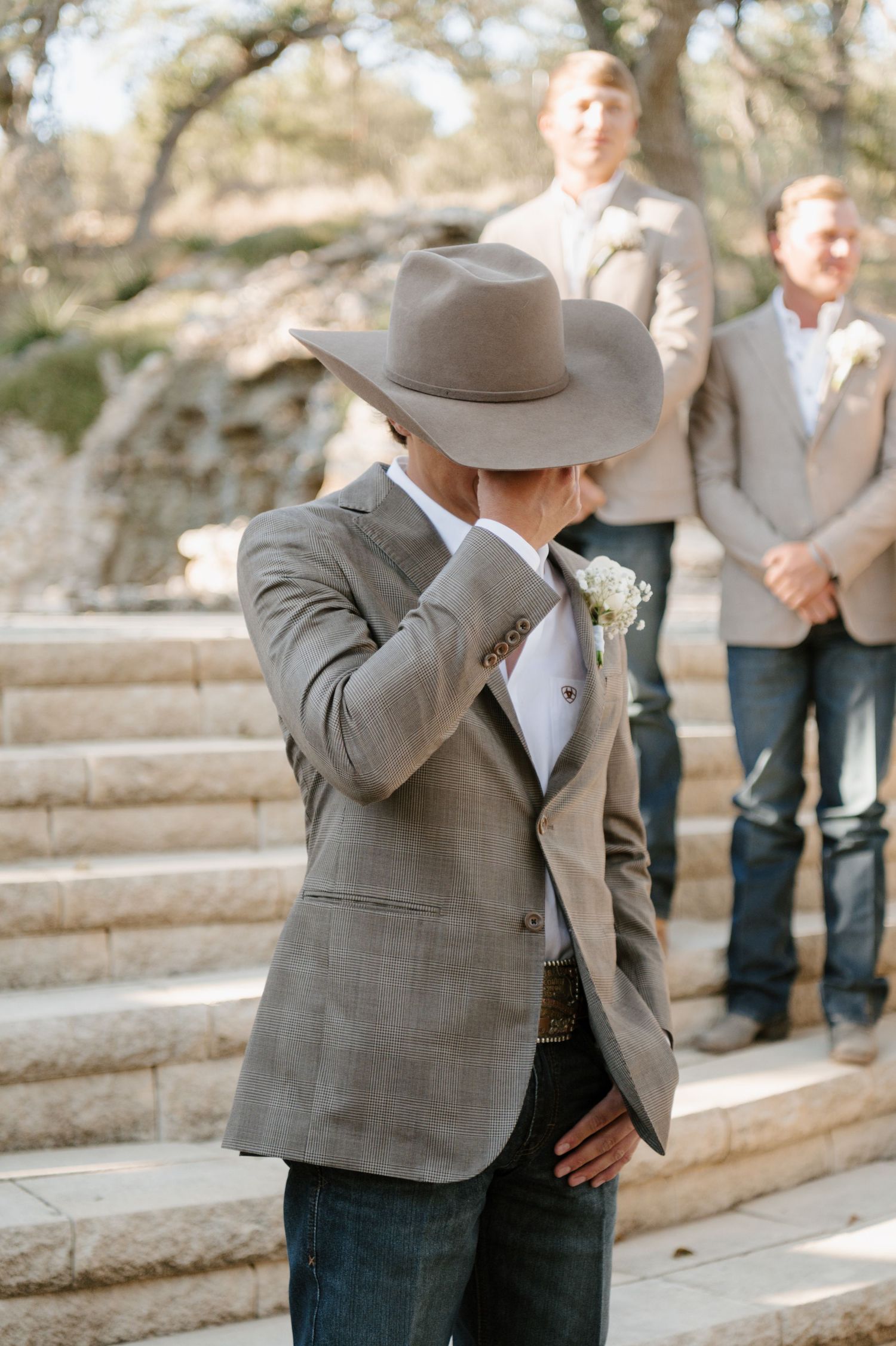 A western-style wedding first look with a groom in a cowboy hat and grey suit jacket.