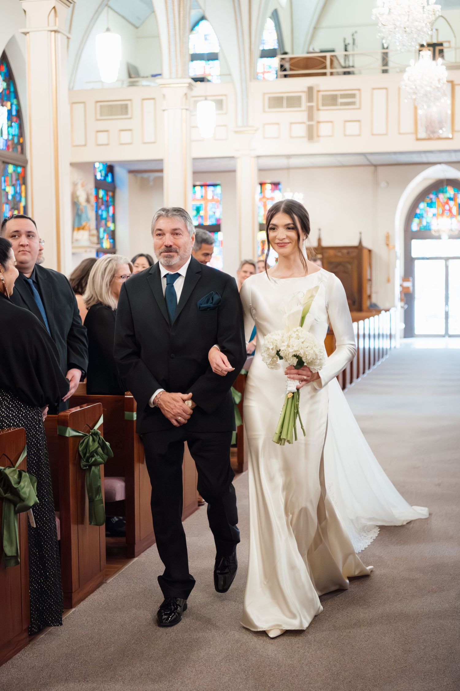 Wedding party walking down the aisle of an elegant white church with ornate architectural details.