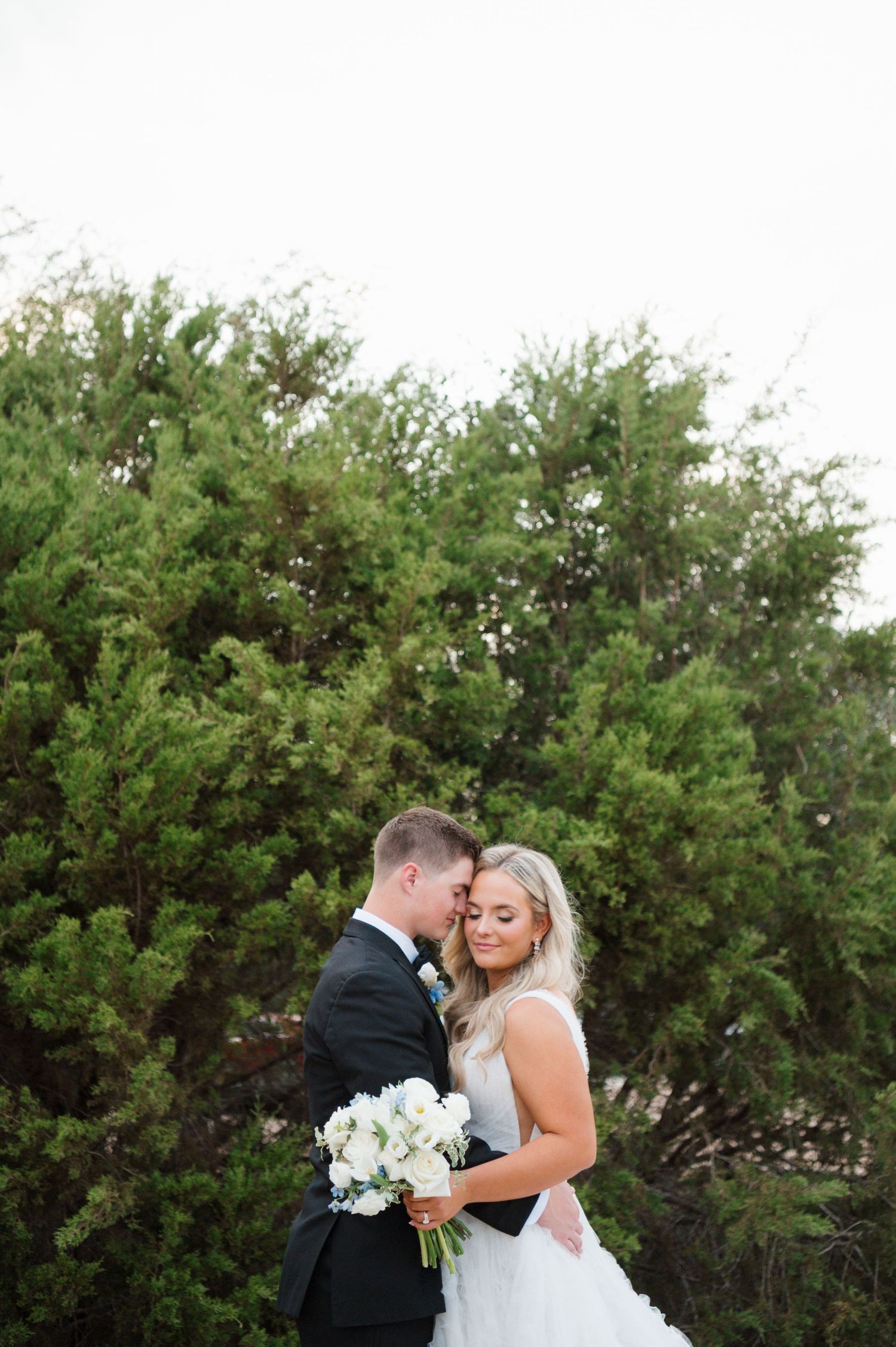 A bride and groom embracing each other in a lush, green outdoor setting.