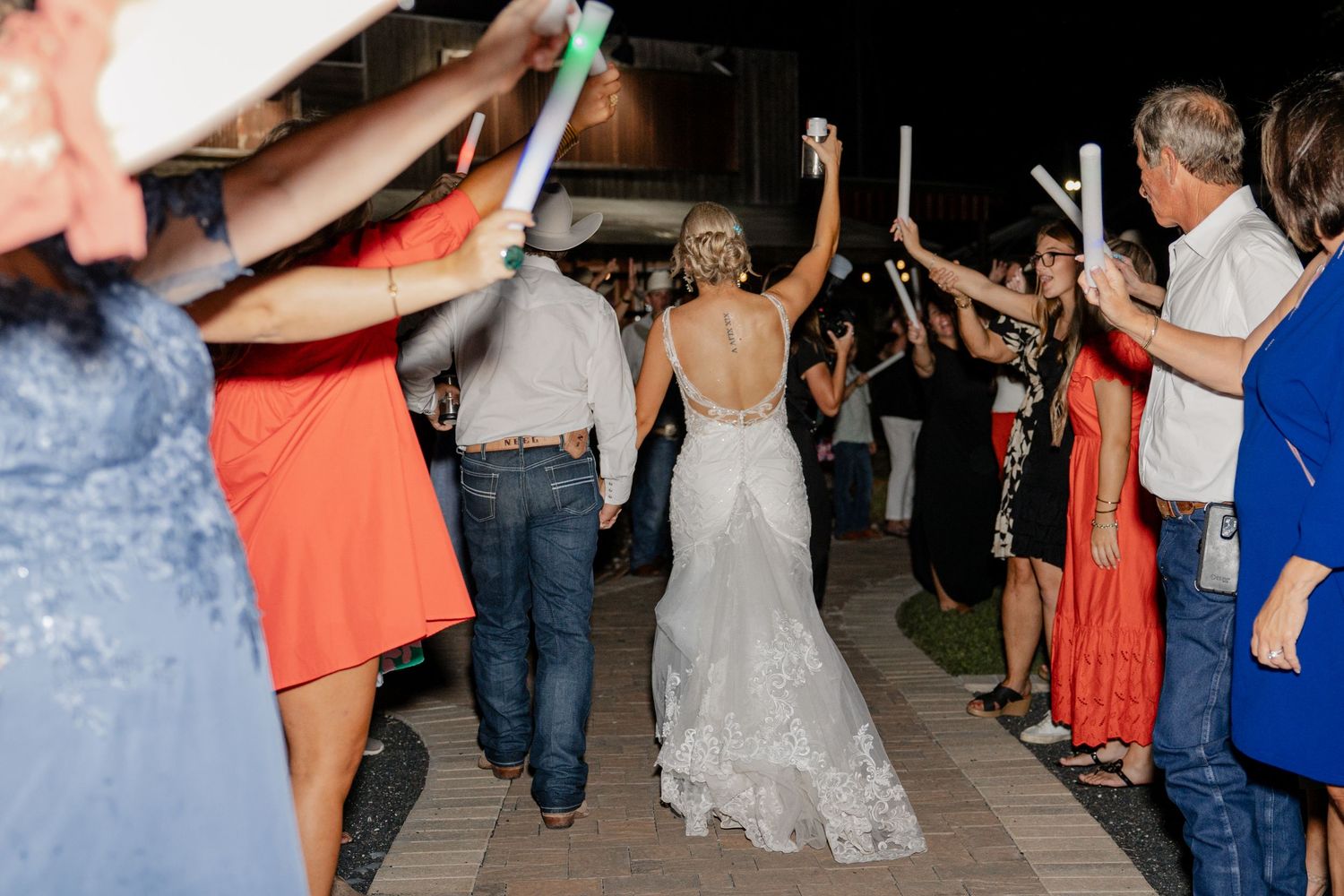 A crowd celebrates on an outdoor dance floor at a wedding reception under string lights.