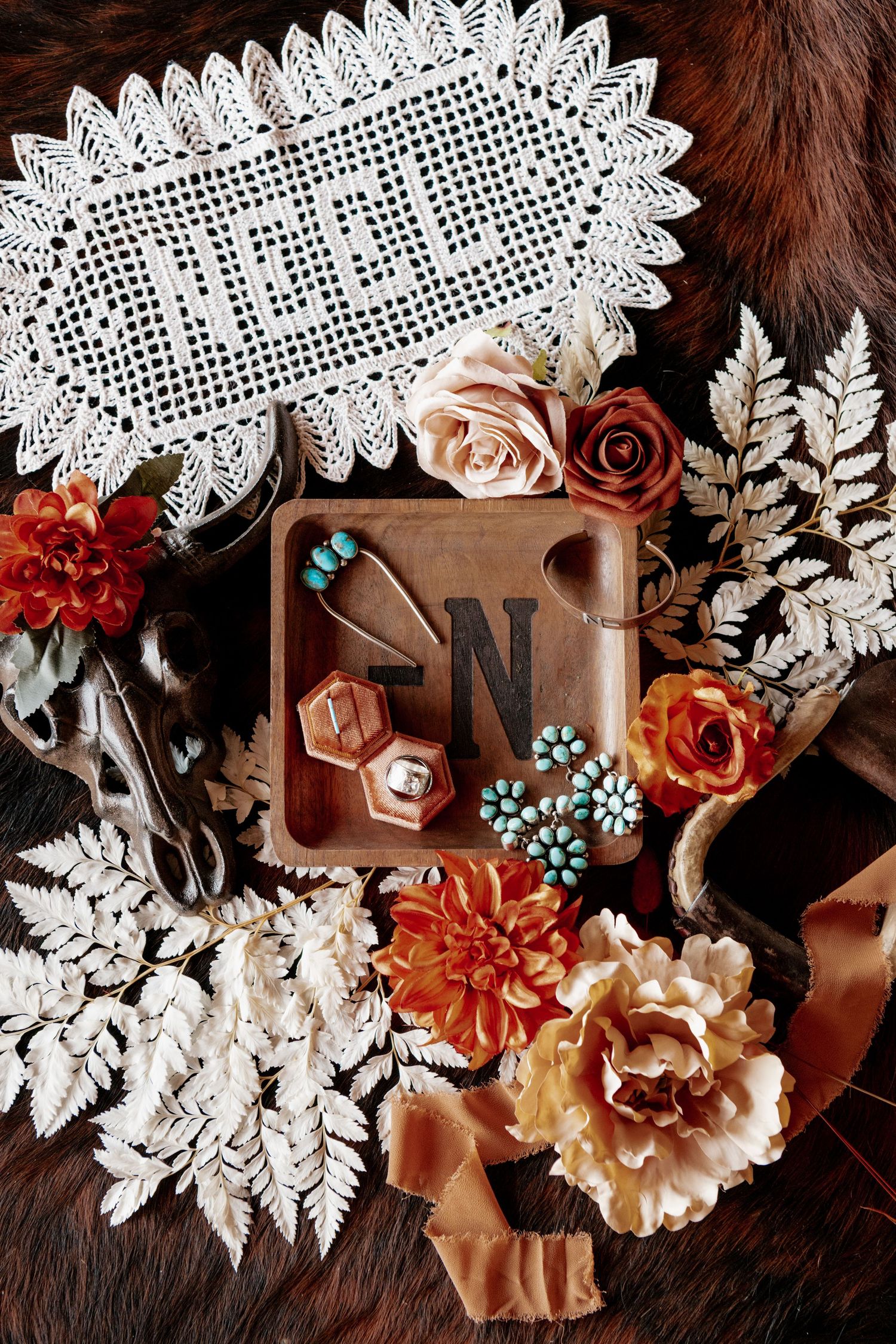 Vintage styled flatlay with lace doily, roses, silver scissors and decorative letter N among white fern leaves.