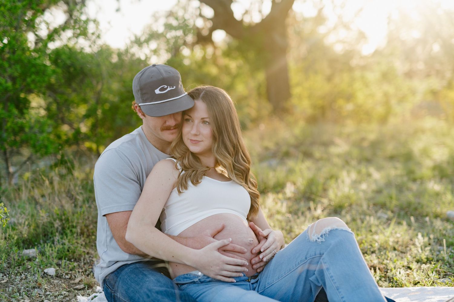 Couple embraces during a sunset maternity photoshoot in a natural outdoor setting.