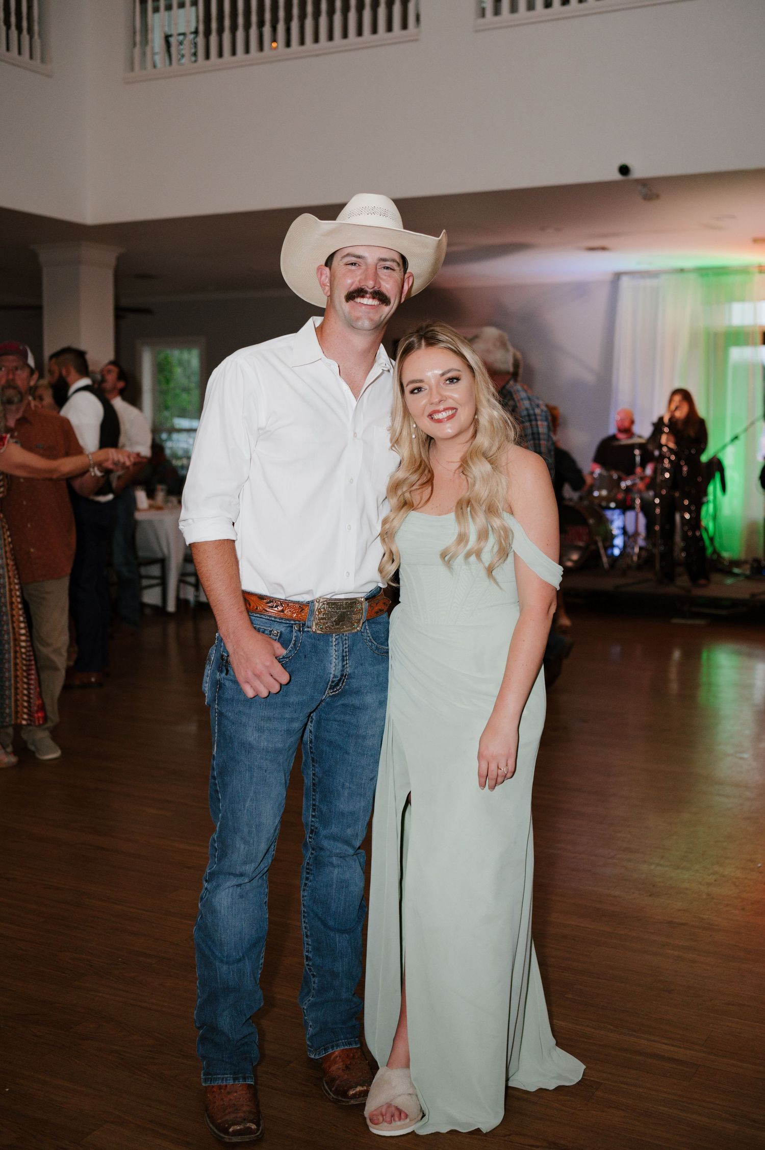 Couple in country western attire dancing together at wedding reception on wooden floor.