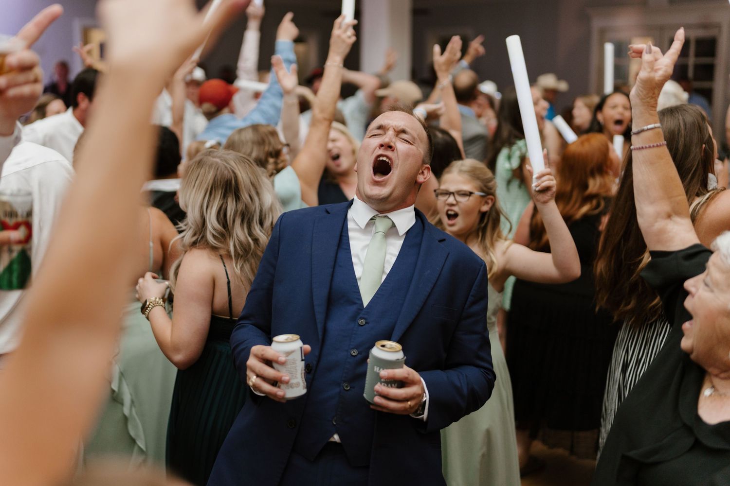 Energetic crowd of wedding guests dancing and celebrating with glow sticks.