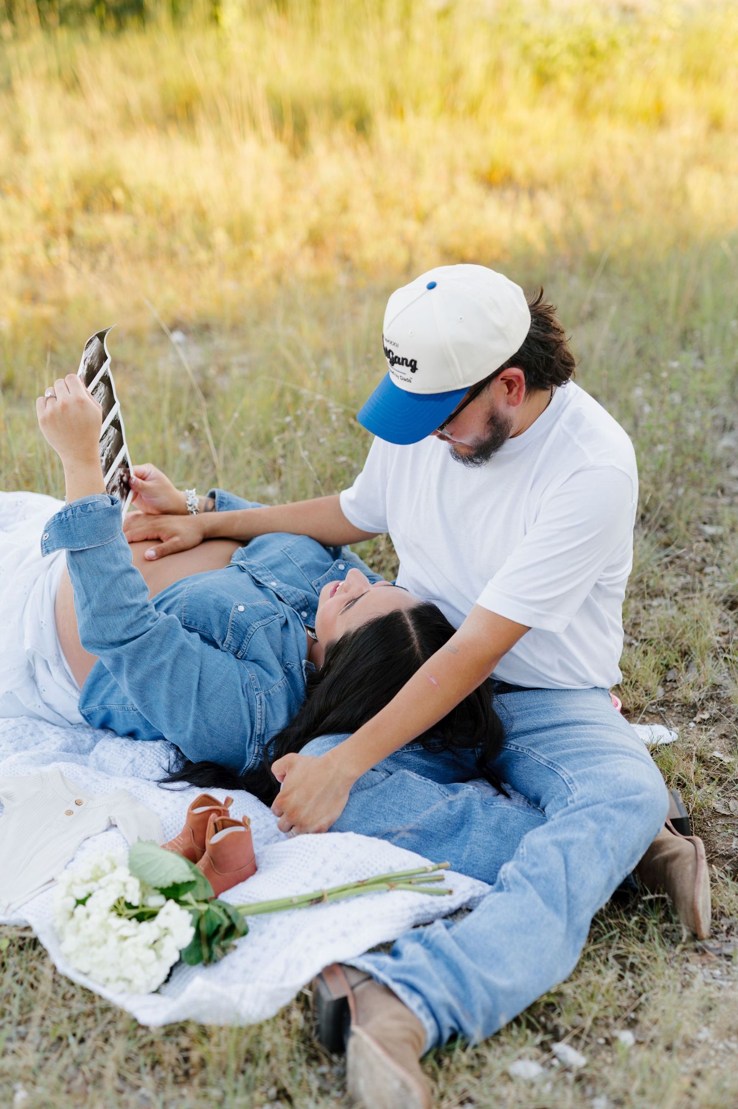 Two people relaxing on a blanket in a grassy field during golden hour.