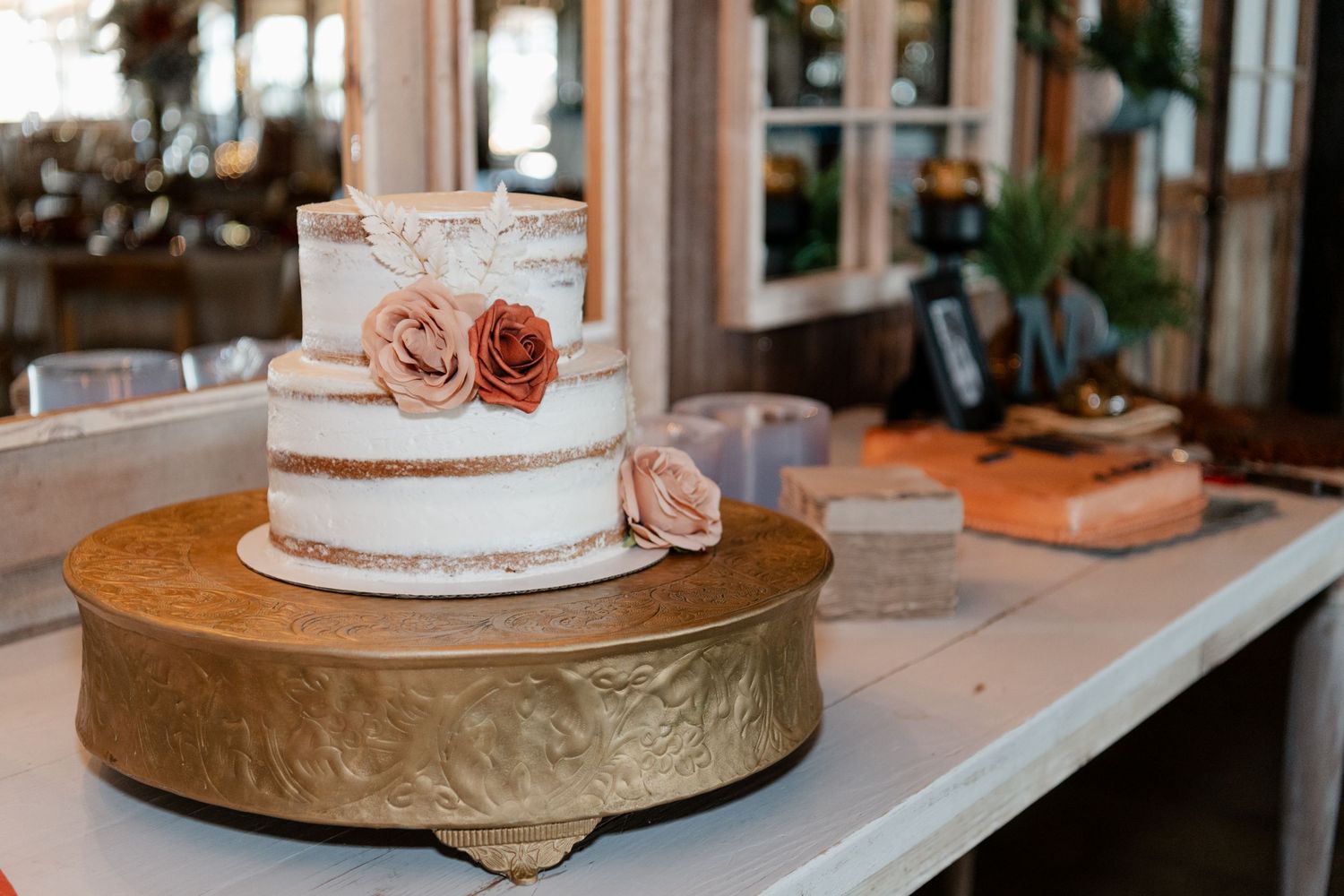 Simple white wedding cake with pink roses on a gold cake stand.