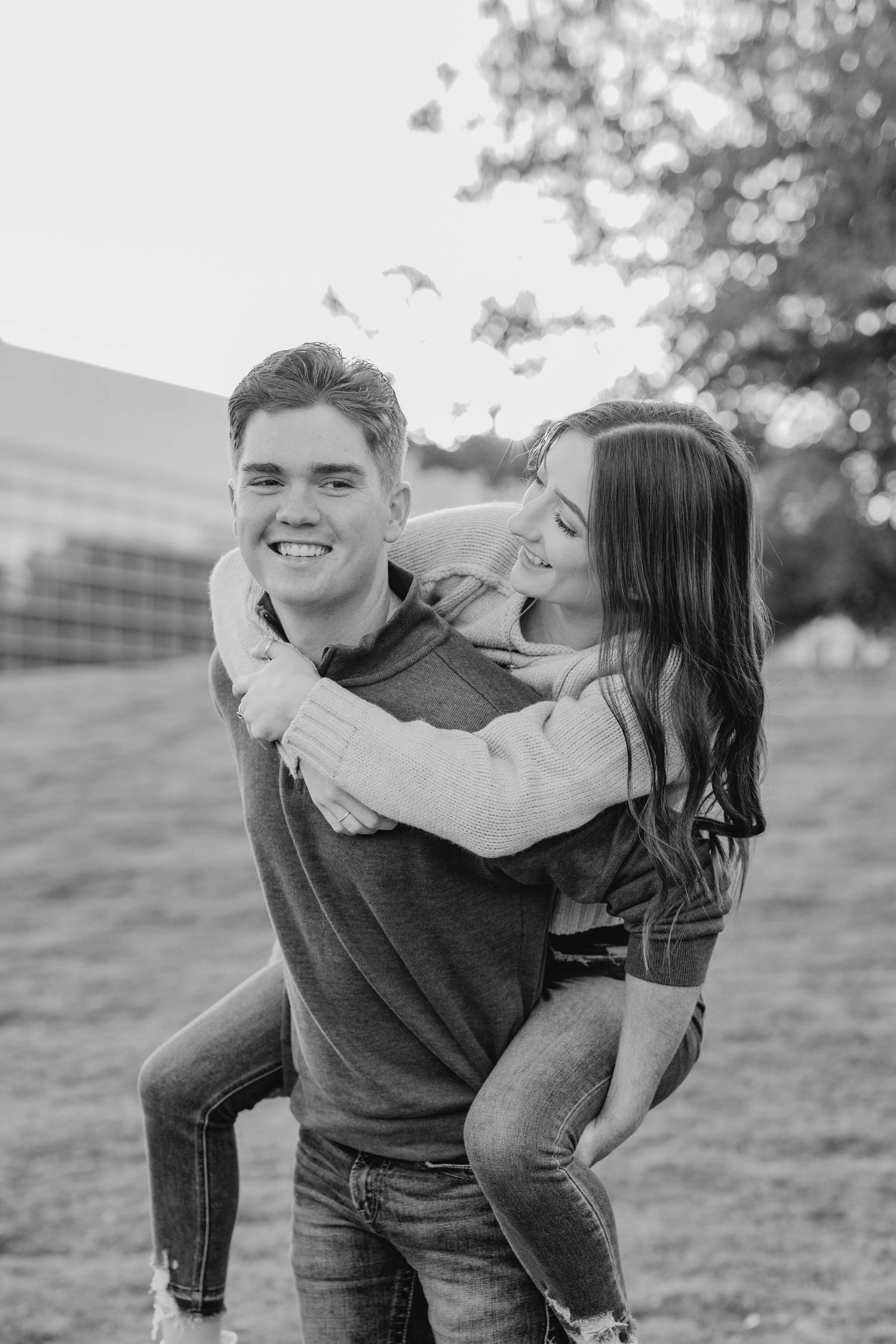 A black and white photo of a couple sharing a playful piggyback ride outdoors.