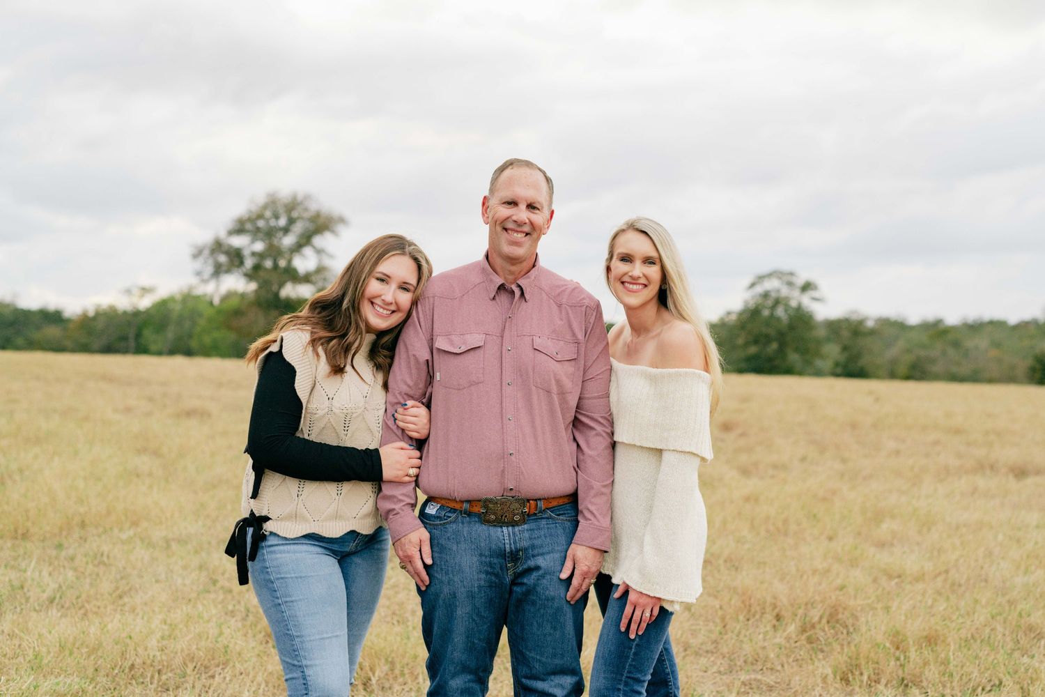 Portrait of three people standing close together in a field during golden hour.