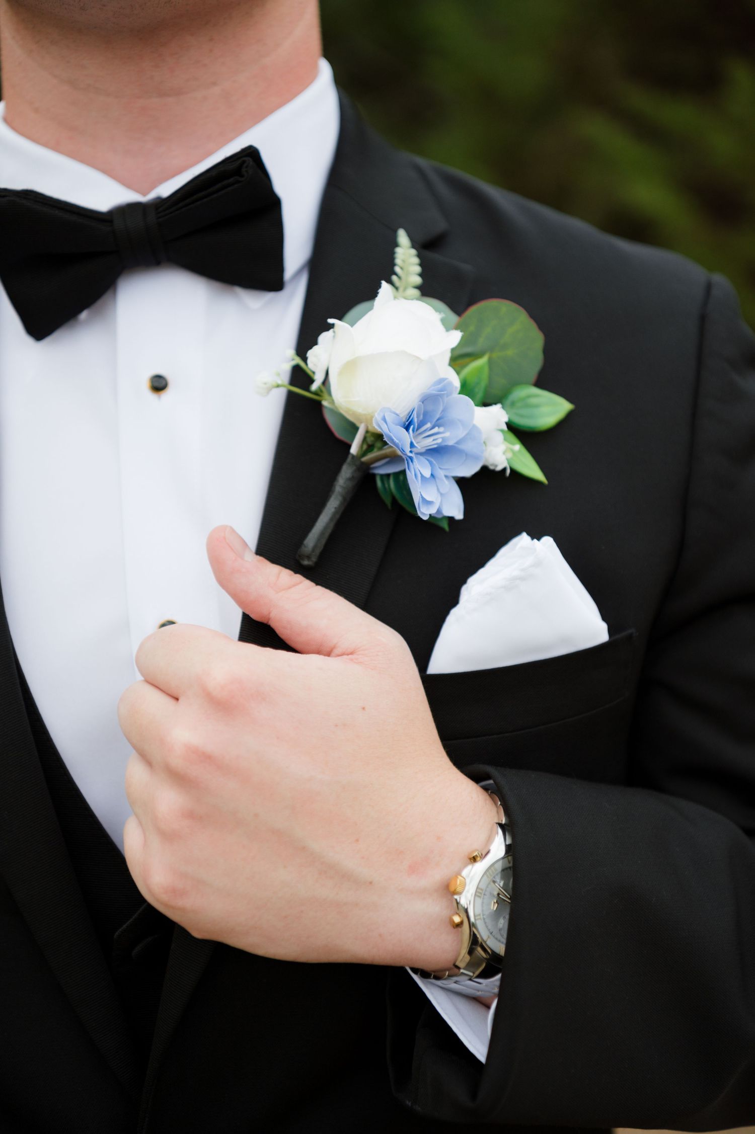 A man in a tuxedo with a bow tie and boutonniere stands with his hand in his pocket.